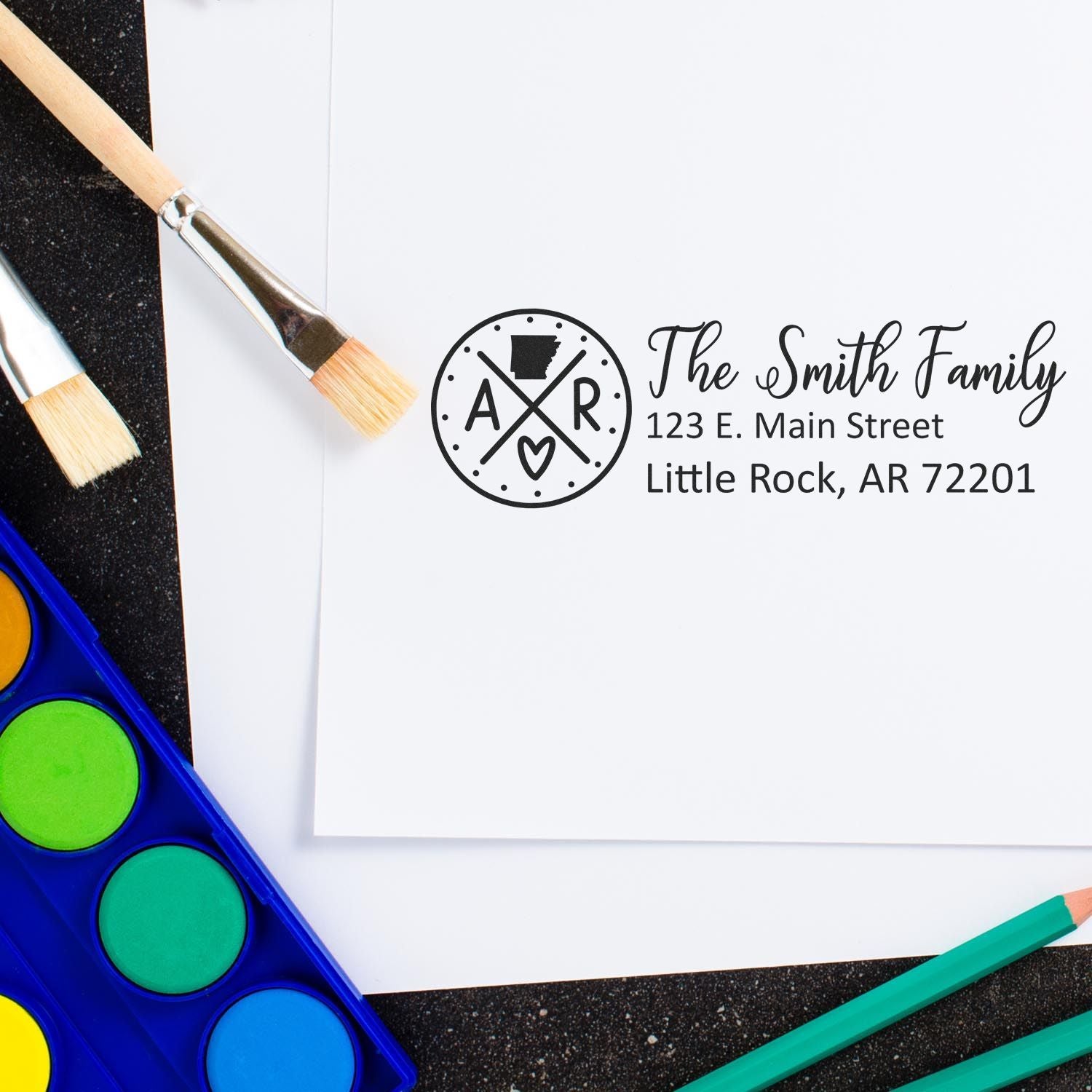 Arkansas State Pride Customized Address Stamp on white paper, surrounded by paintbrushes and watercolor paints, featuring a personalized address for The Smith Family in Little Rock, AR.