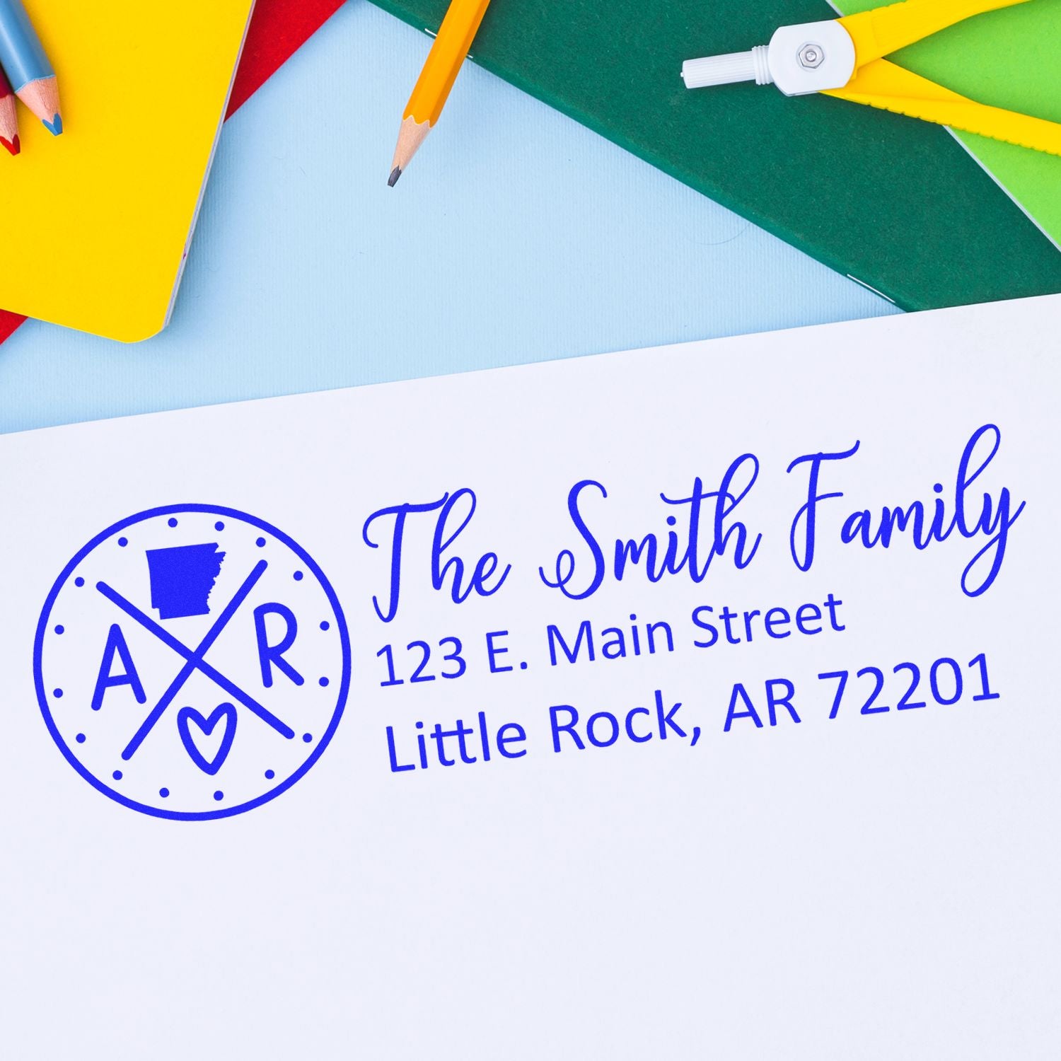 Arkansas State Pride Customized Address Stamp featuring a circular design with AR and a heart, personalized with The Smith Family and an address. Set against a colorful background with stationery.