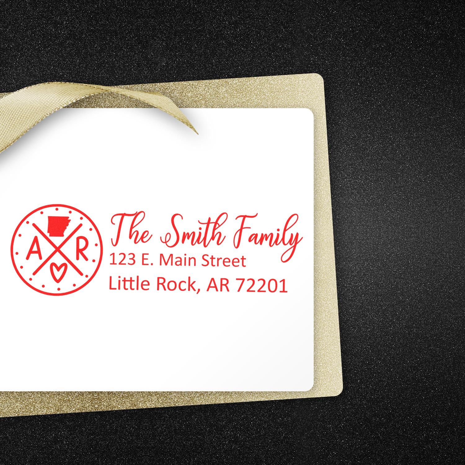 PSI Pre-Inked Arkansas State Pride Customized Address Stamp on a white card with red text, featuring a state-themed design. The card is placed on a glittery black surface with a gold ribbon.