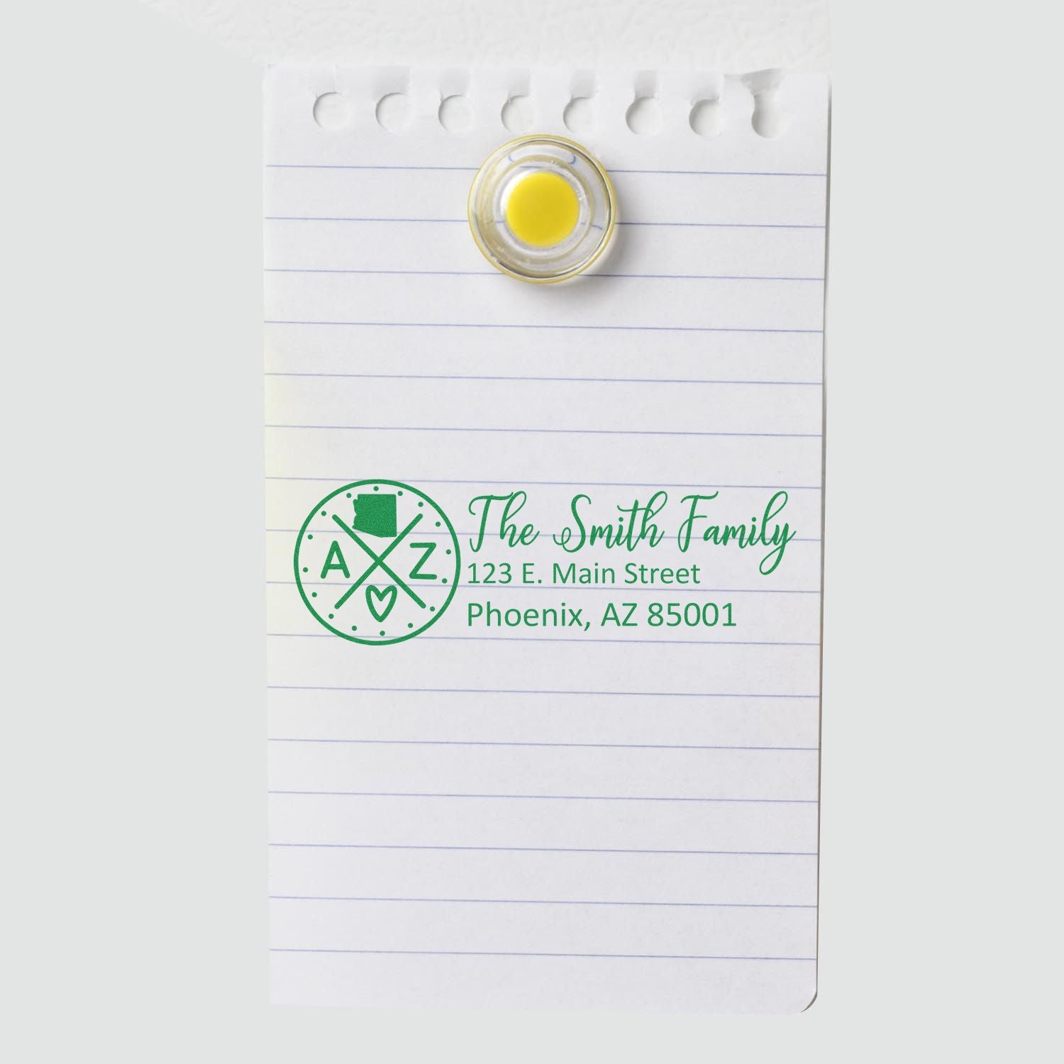 Slim Arizona Customized Pre-Inked Address Stamp on lined paper, displaying The Smith Family, 123 E. Main Street, Phoenix, AZ 85001 in green ink, secured with a round magnet.