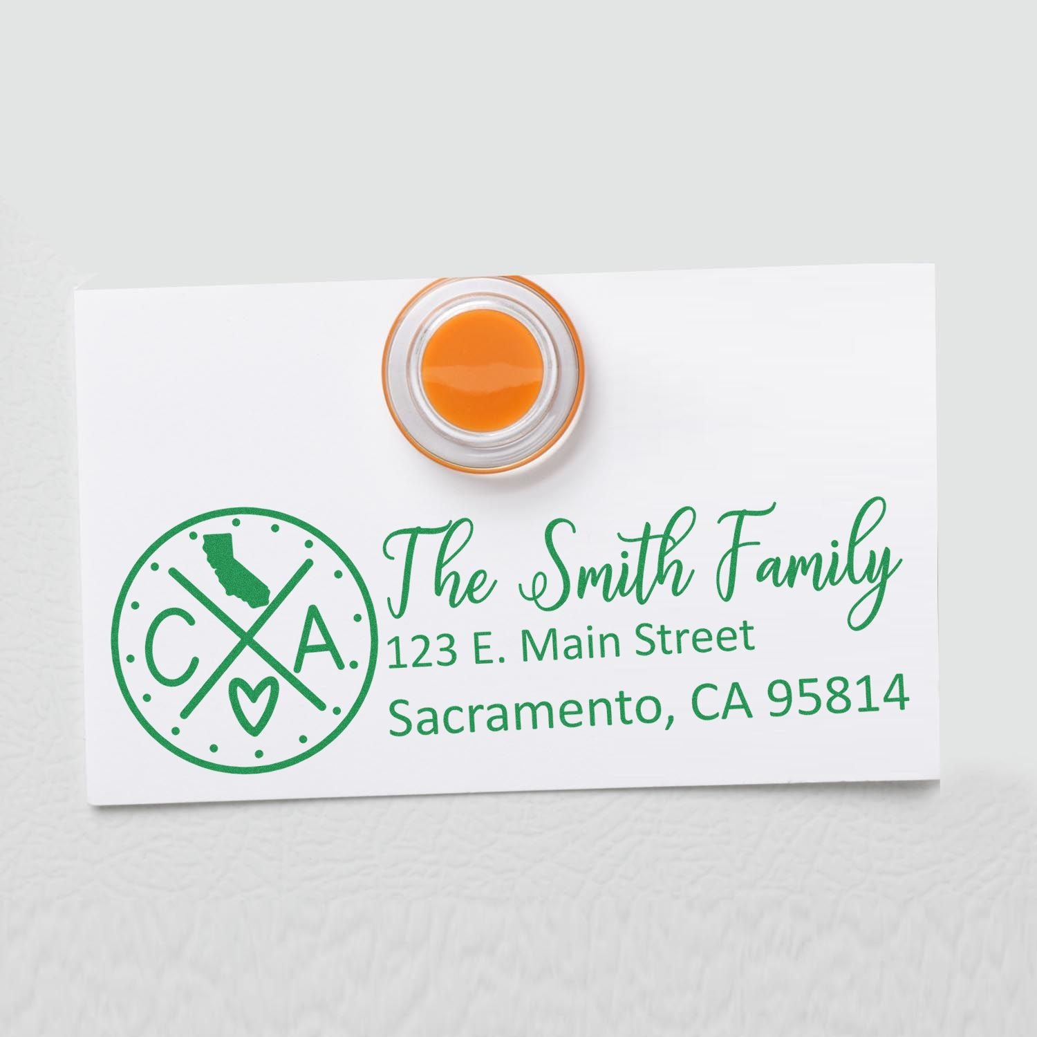 California State Pride Customized Address Stamp on a white card with green text, featuring a California map icon and personalized address for the Smith Family in Sacramento. Orange magnet holds the card.