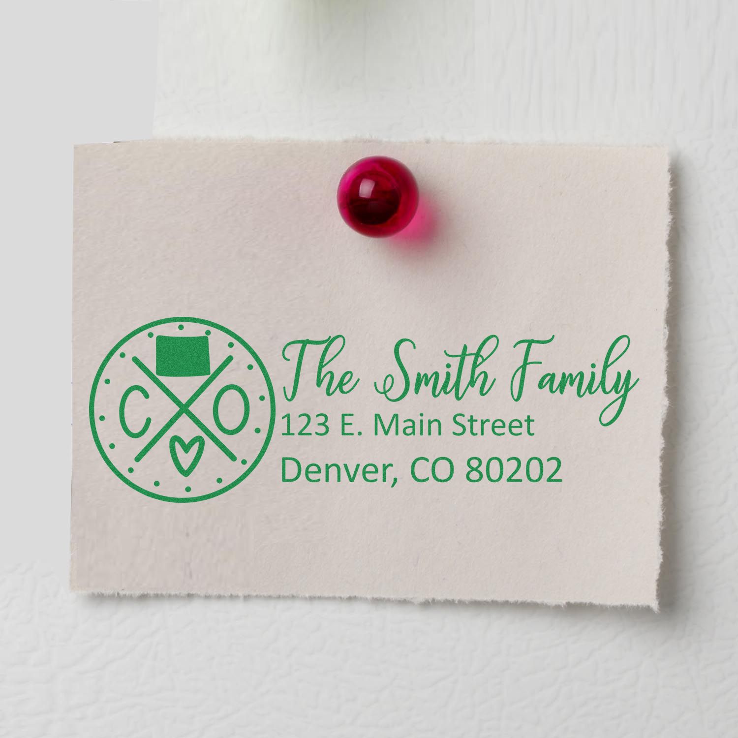 PSI Pre-Inked Colorado State Pride Customized Address Stamp on paper with green ink, featuring a family name and Denver address, pinned with a red pushpin.