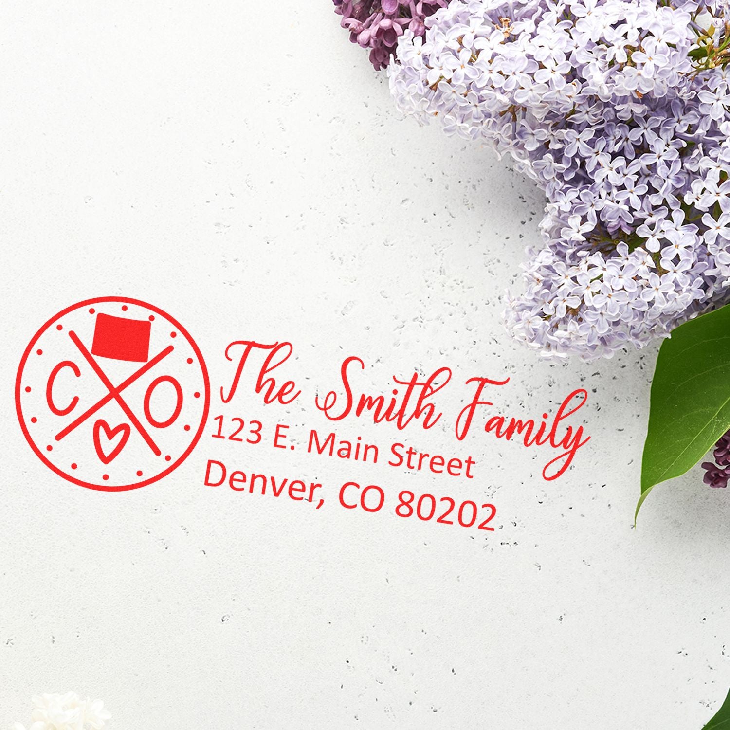 Slim Colorado Customized Pre-Inked Address Stamp in red ink on white paper, featuring a family name and address, surrounded by lilac flowers and green leaves.