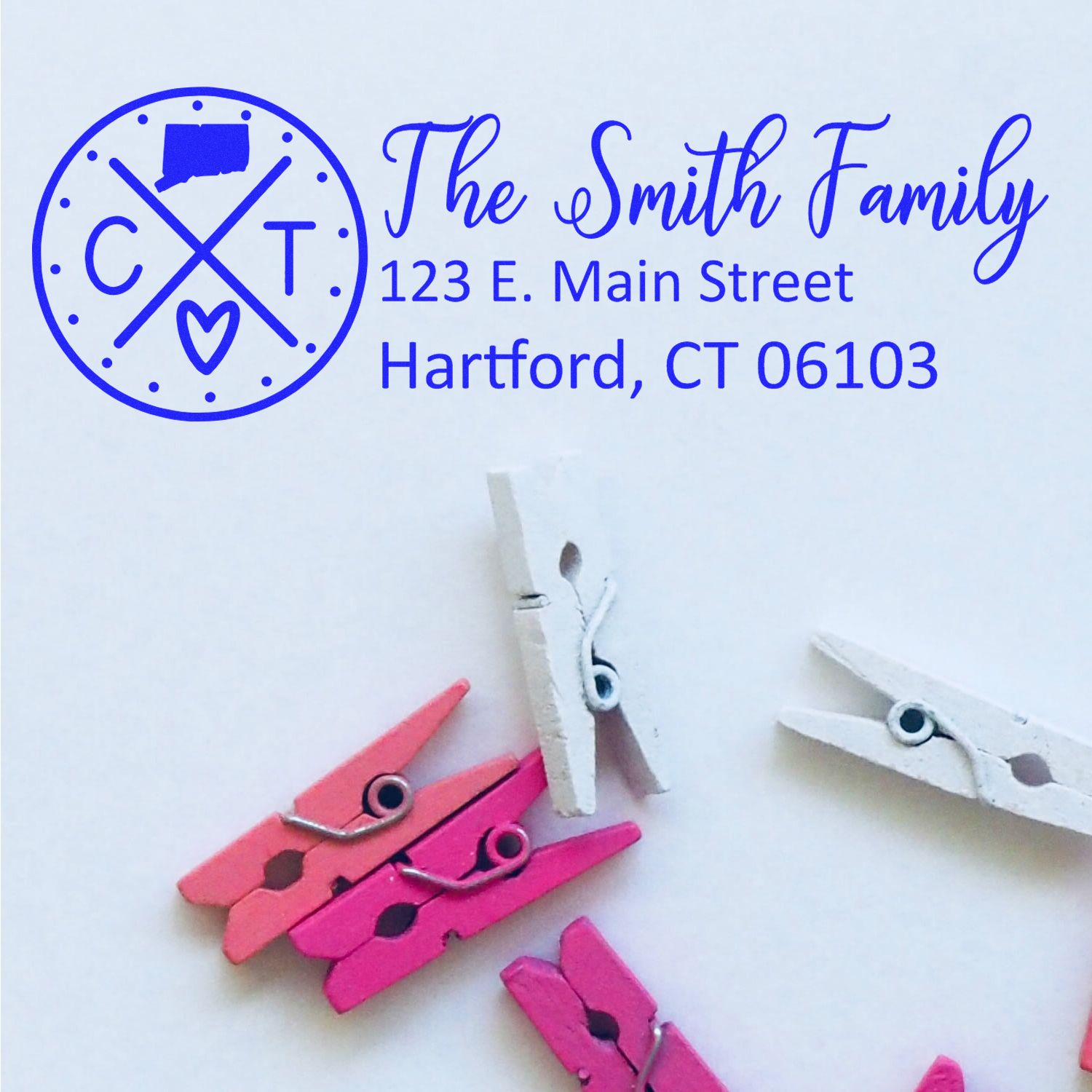 Image of a Connecticut State Pride Customized Address Stamp with The Smith Family and address in blue ink. Pink and white clothespins are scattered below on a white background.