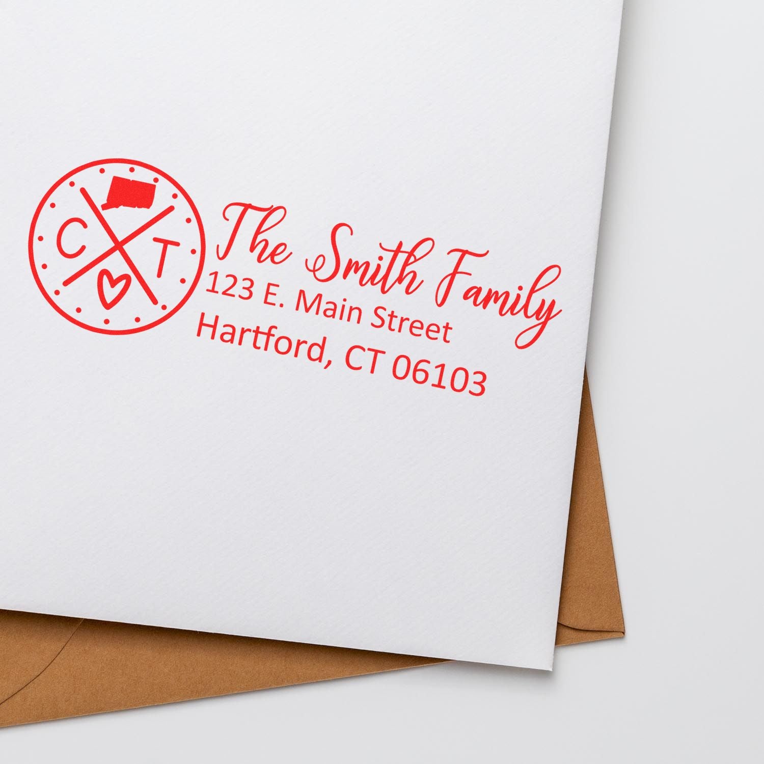 Slim Connecticut Customized Pre-Inked Address Stamp on white envelope with red ink, featuring a circular design and personalized address for The Smith Family, Hartford, CT. Brown envelope underneath.