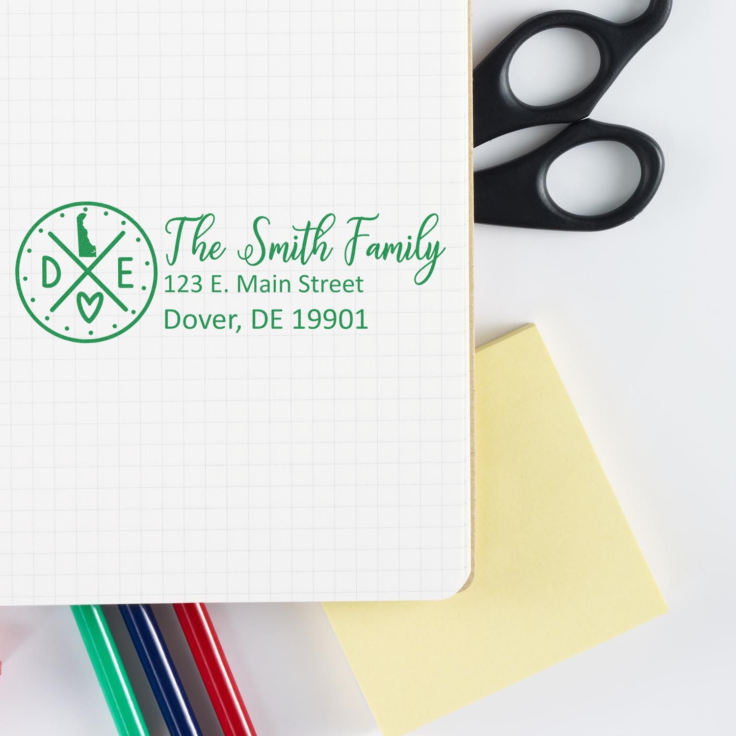 Delaware State Pride Customized Address Stamp on a notebook with scissors, sticky notes, and colored pens. The stamp displays The Smith Family and an address in green ink.