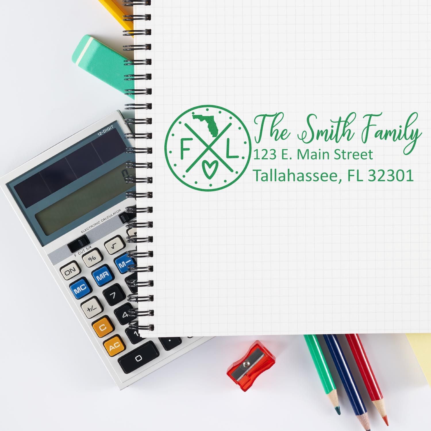 PSI Pre-Inked Florida State Pride Customized Address Stamp on a notebook, surrounded by a calculator, colored pencils, and paper clips, showcasing a personalized address for the Smith Family in green ink.