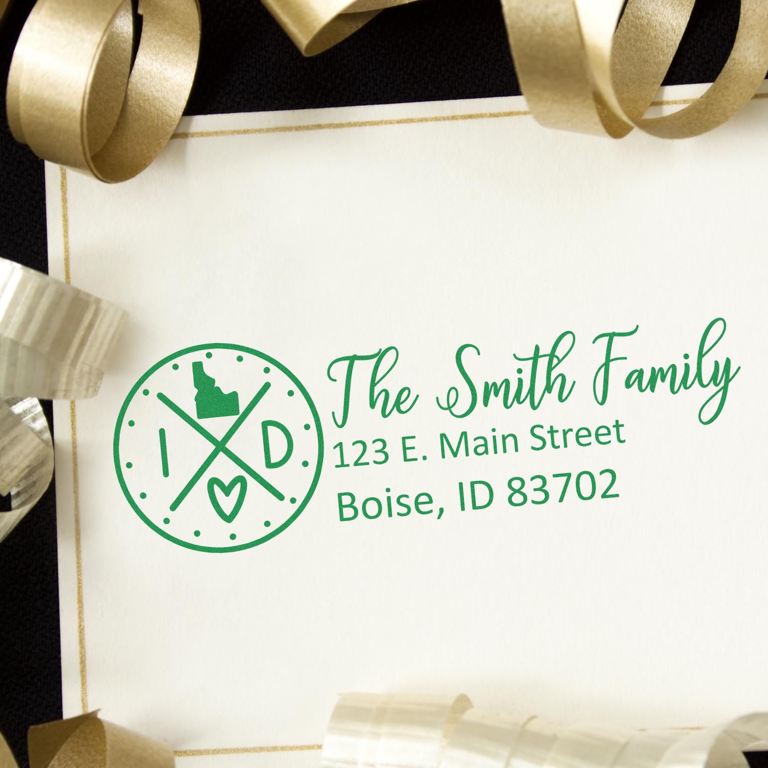 Idaho State Pride Customized Address Stamp on an envelope with gold ribbons. Features a green design with the state outline, heart, and initials, personalized with The Smith Family and Boise address.