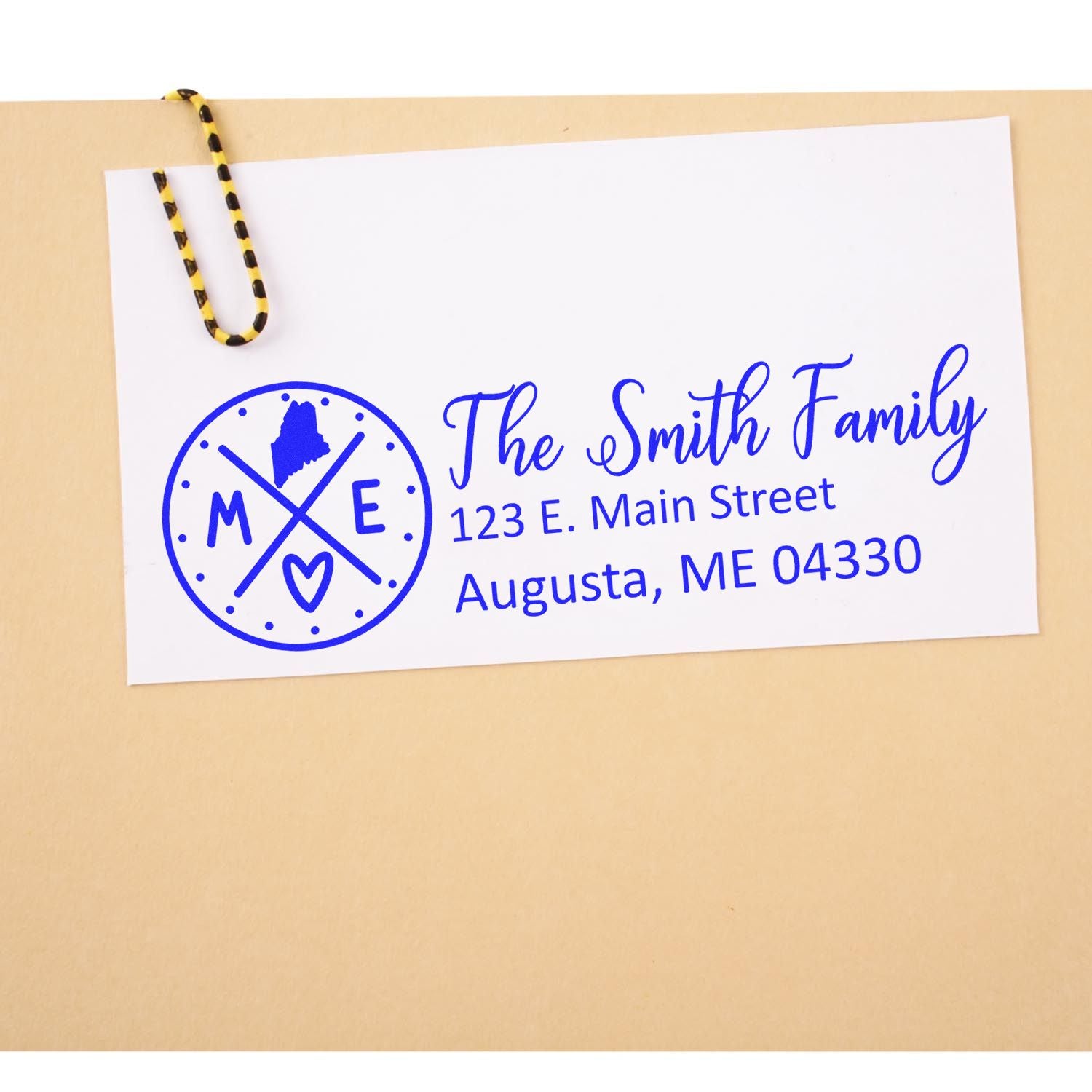 Slim Maine Customized Pre-Inked Address Stamp on an envelope with The Smith Family, 123 E. Main Street, Augusta, ME 04330 in blue ink, featuring a Maine state outline and heart design.