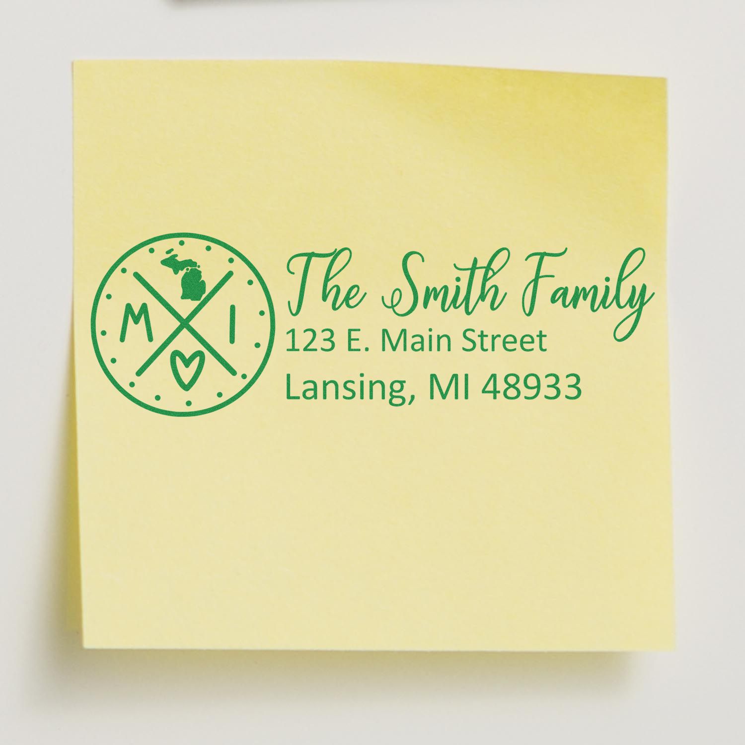 Yellow sticky note with a green Michigan State Pride Customized Address Stamp featuring The Smith Family and an address in Lansing, MI. The design includes a Michigan map and heart.