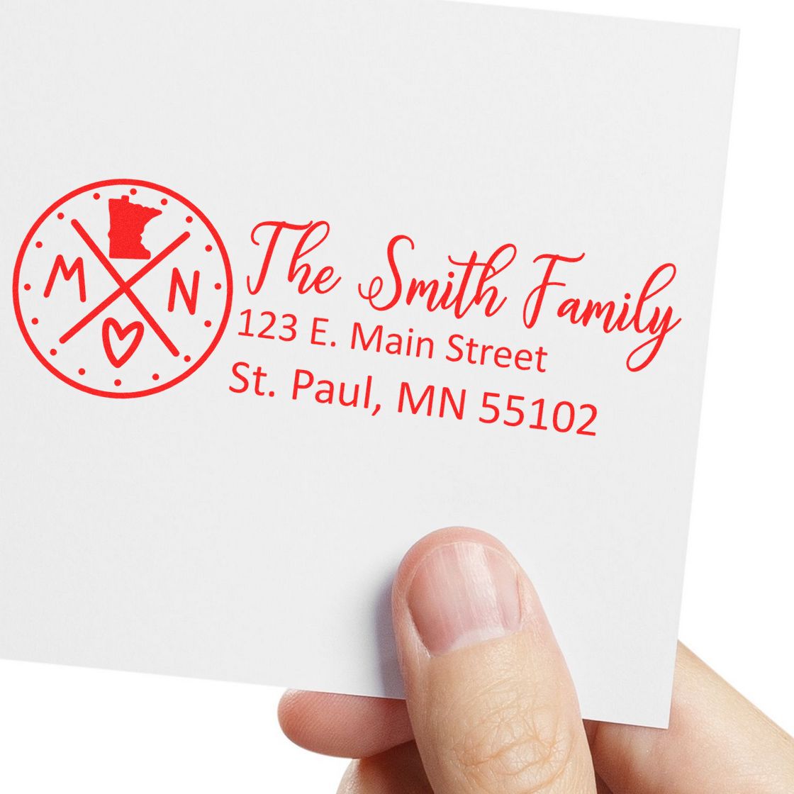 A hand holds a card stamped with the Self-Inking State Love of Minnesota Custom Address Stamp, featuring a red design with MN and a heart, displaying an address in St. Paul, MN.