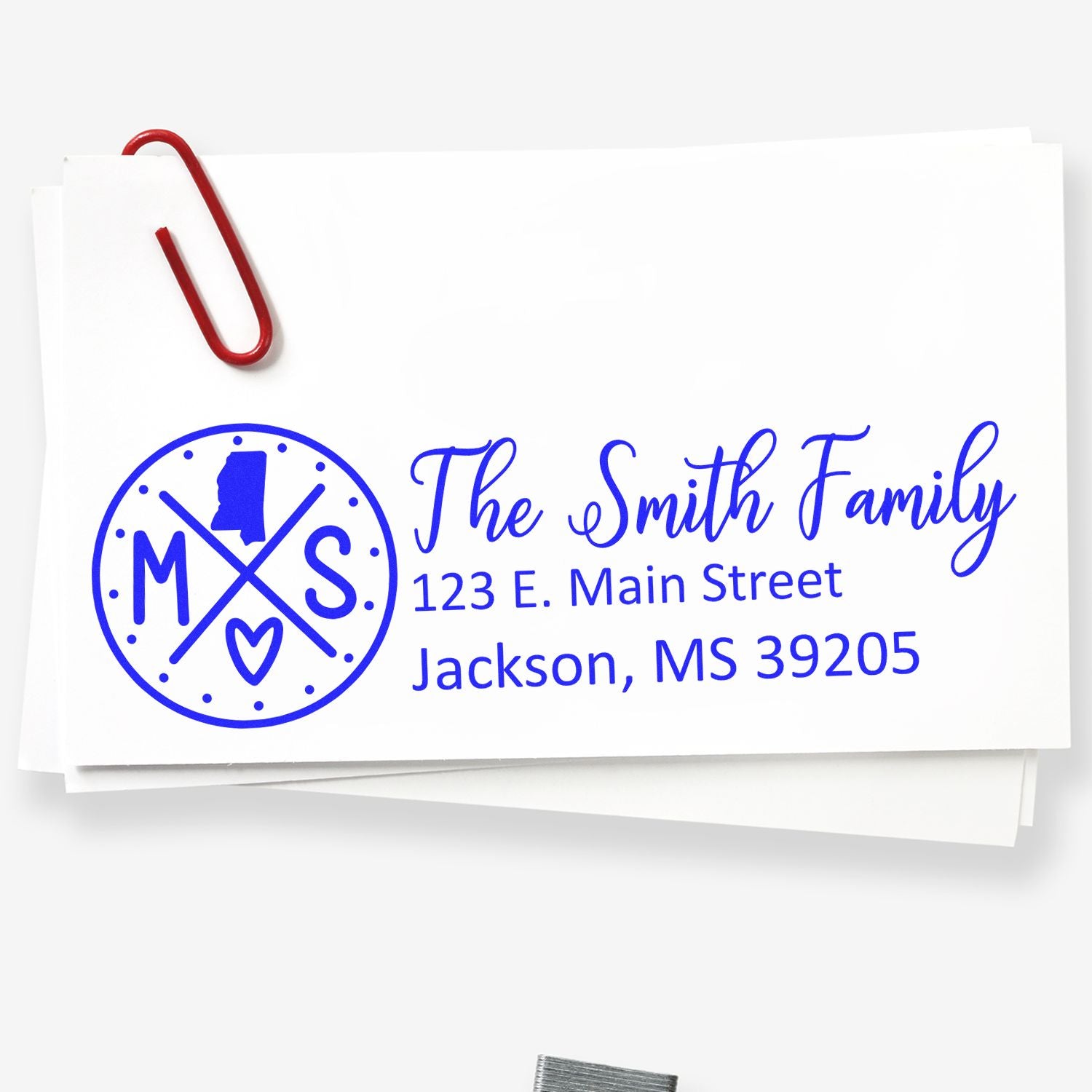 PSI Pre-Inked Mississippi State Pride Customized Address Stamp on white envelope with blue ink, featuring a circular design with MS and a heart, alongside a family name and address.