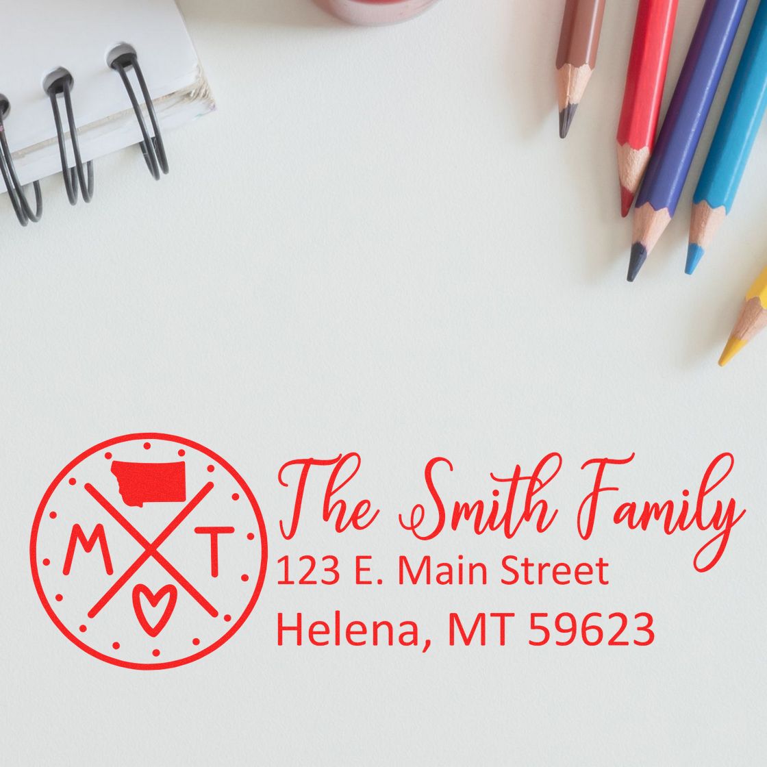 Self-Inking State Love of Montana Custom Address Stamp featuring a red design with 'MT' and a heart, personalized with 'The Smith Family' address, surrounded by colored pencils and a notebook.