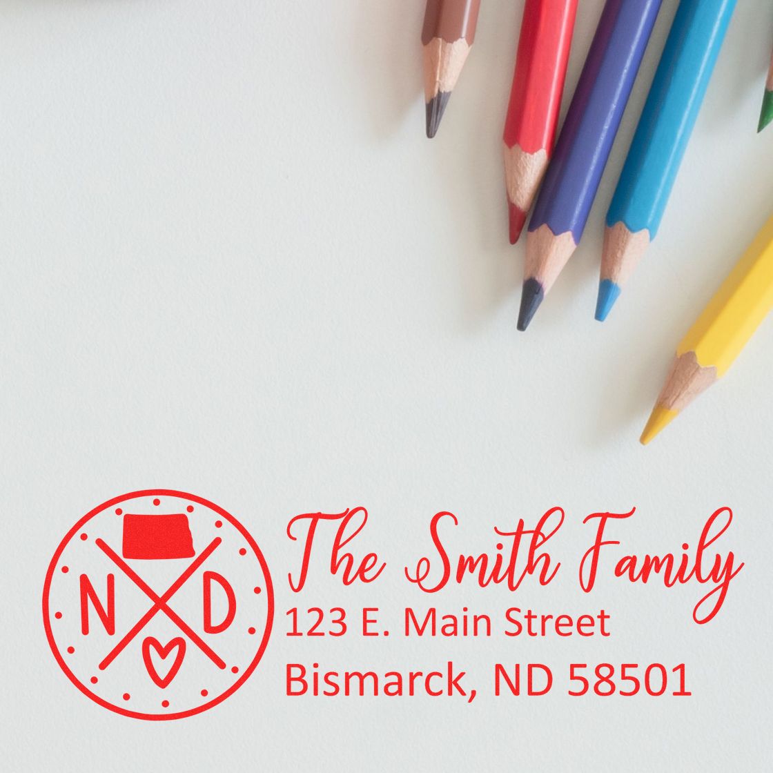 PSI Pre-Inked North Dakota State Pride Customized Address Stamp with The Smith Family and address in red ink, next to colorful pencils on a white background.