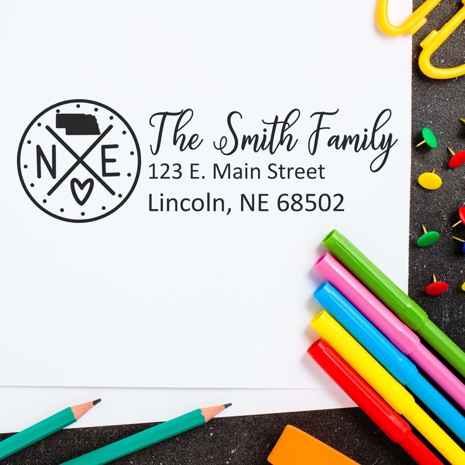 Self-Inking State Love of Nebraska Custom Address Stamp on white paper with colorful pens and push pins nearby, displaying The Smith Family, 123 E. Main Street, Lincoln, NE 68502.