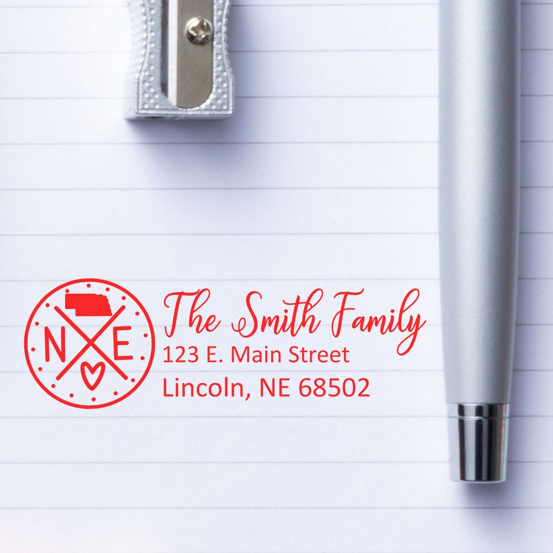 PSI Pre-Inked Nebraska State Pride Customized Address Stamp on lined paper with a silver pen and pencil sharpener, featuring a red design with The Smith Family and a Nebraska state outline.