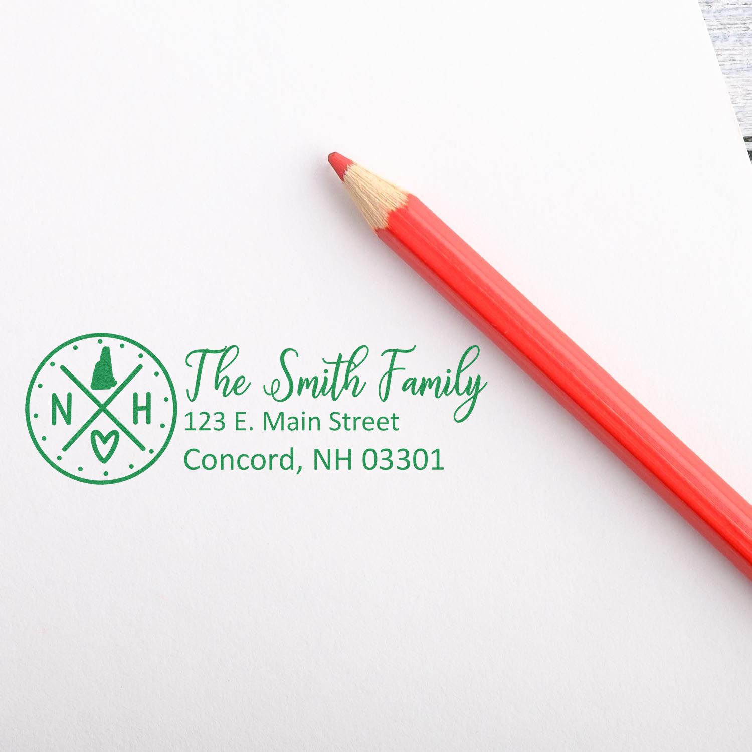 New Hampshire State Pride Customized Address Stamp on white paper with a red pencil. The stamp features a personalized address and NH state symbols, ideal for adding a personal touch to mail.