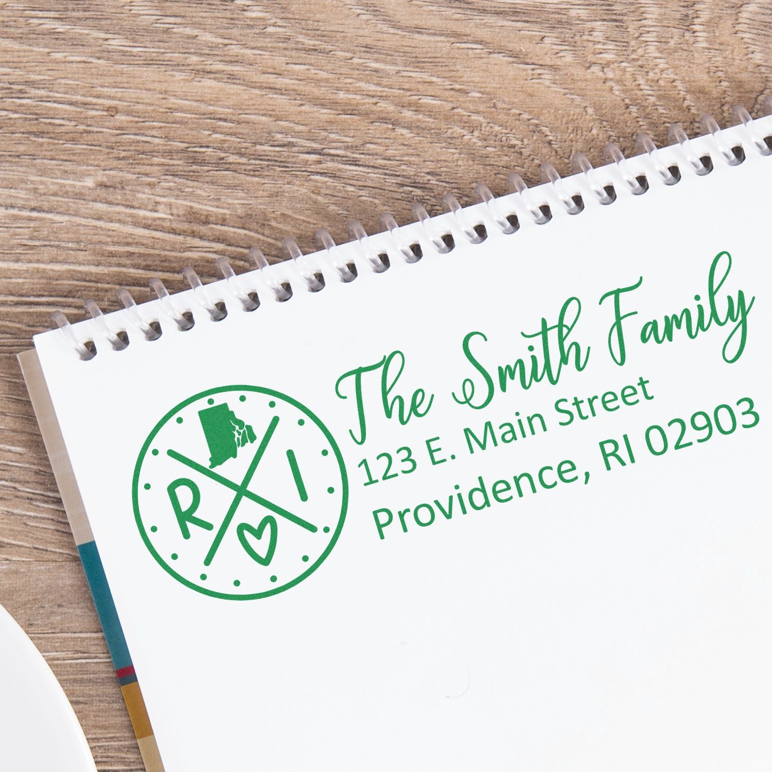 Rhode Island State Pride Customized Address Stamp on a notebook, featuring a circular design with RI and a heart, alongside a sample address for The Smith Family in green ink.