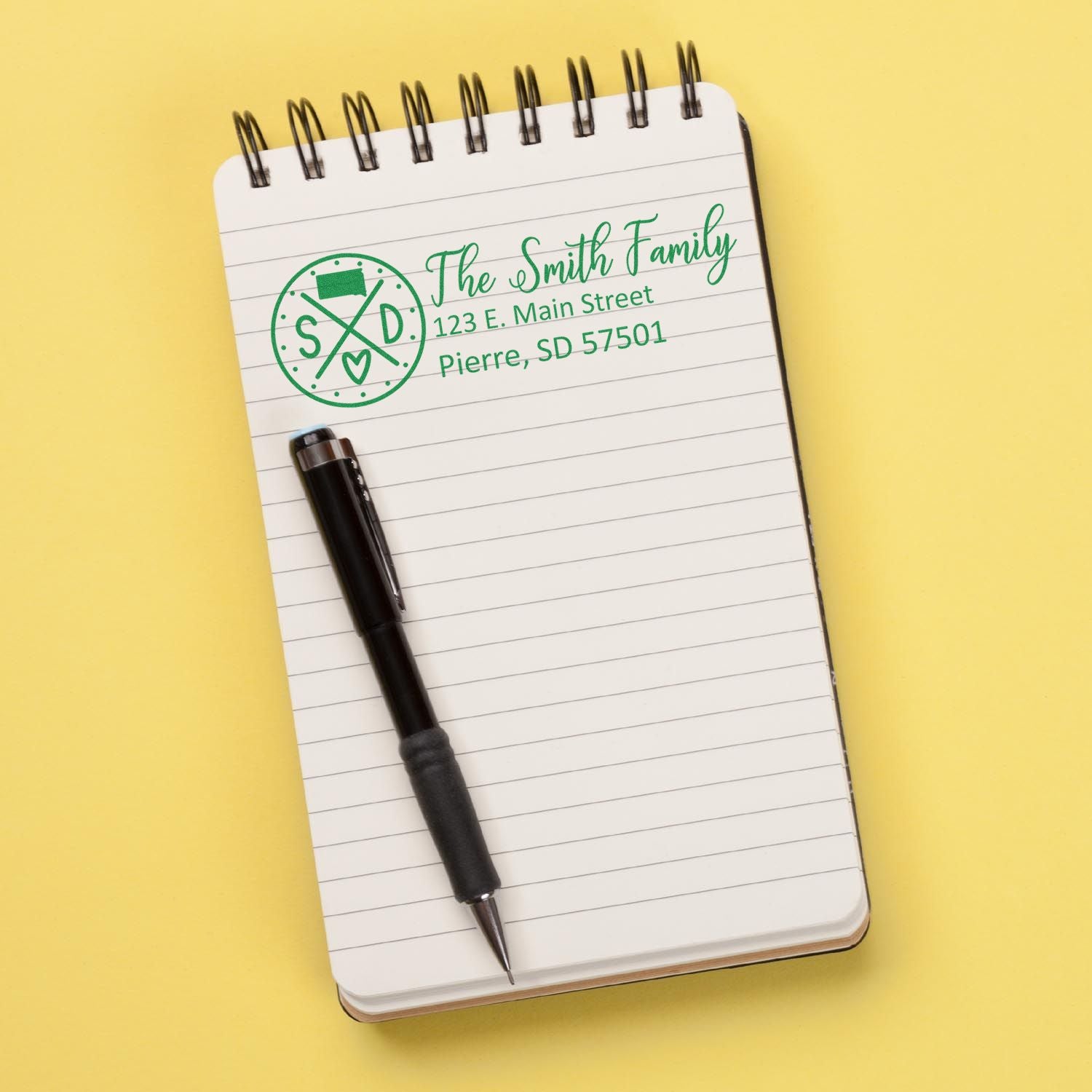 South Dakota State Pride Customized Address Stamp on a notepad with a pen, displaying The Smith Family, 123 E. Main Street, Pierre, SD 57501 in green ink.