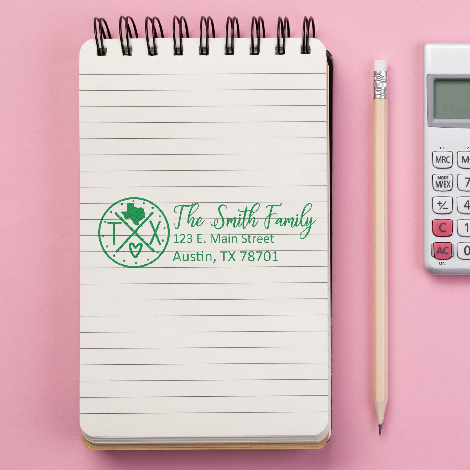 Texas State Pride Customized Address Stamp on a notepad with a pink background, pencil, and calculator. The stamp displays a family name and address in green ink, featuring a Texas-themed design.