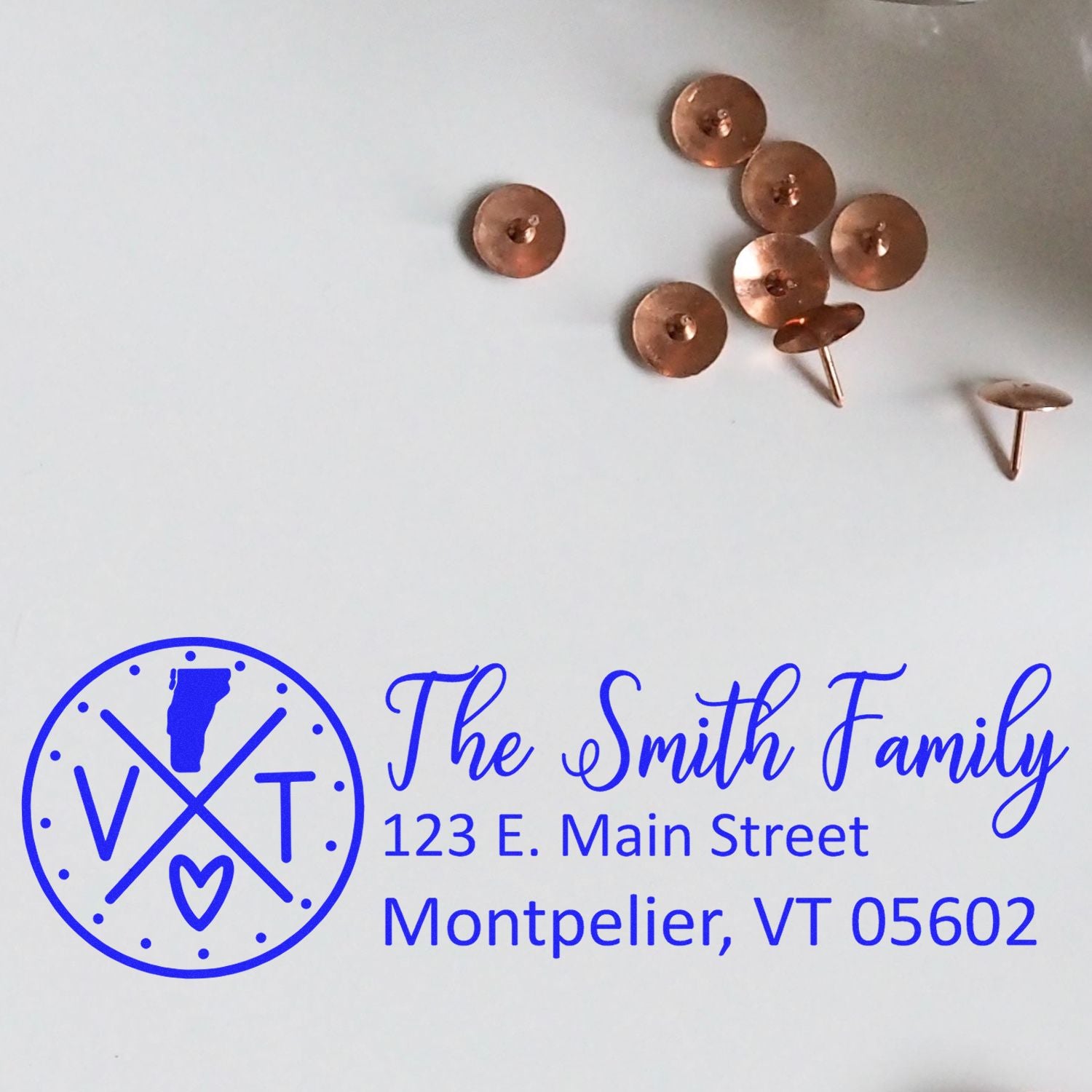 Vermont State Pride Customized Address Stamp featuring a blue design with The Smith Family and Montpelier address, next to copper tacks on a white surface.