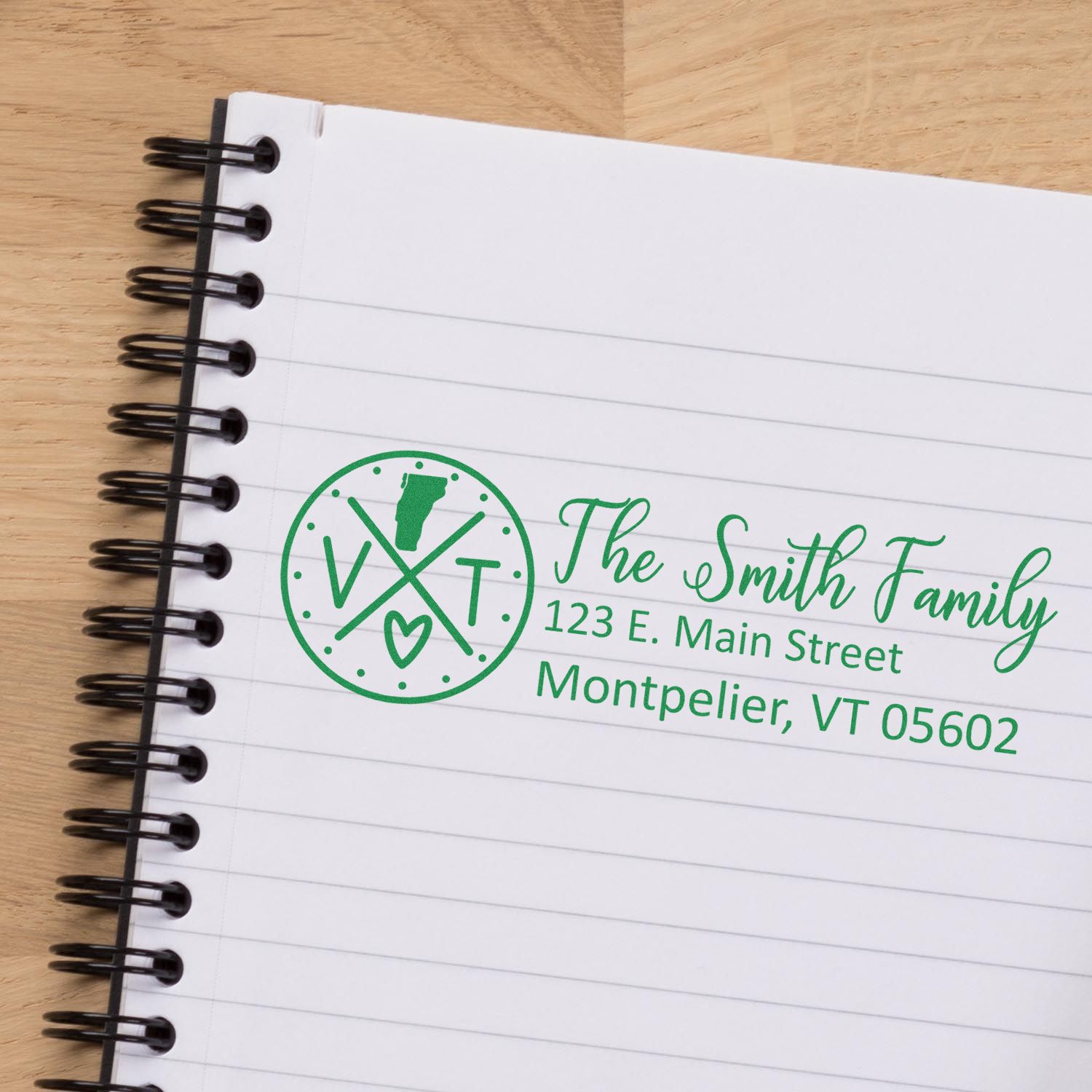 Self-Inking State Love of Vermont Custom Address Stamp on a notebook, displaying The Smith Family, 123 E. Main Street, Montpelier, VT 05602 in green ink with a Vermont state outline and heart.