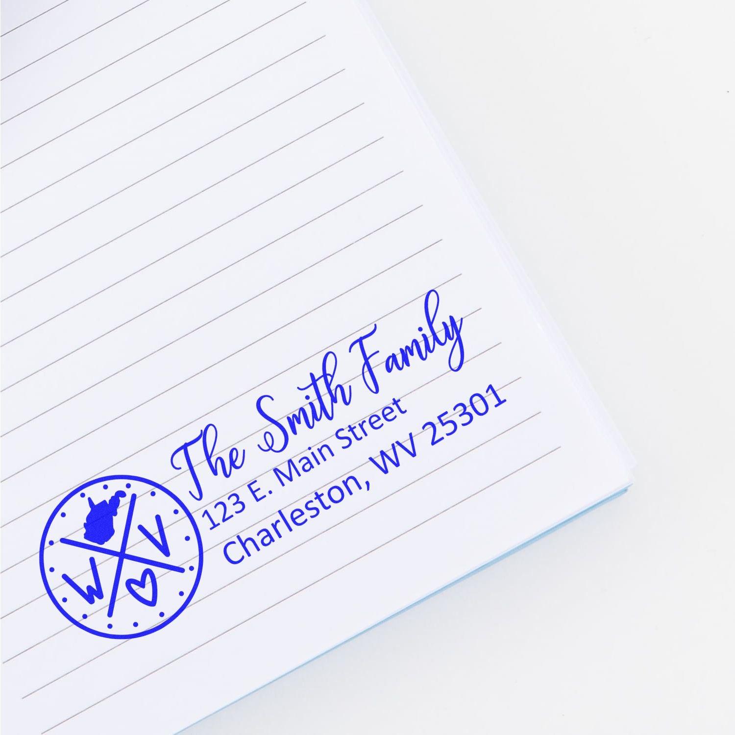 West Virginia State Pride Customized Address Stamp in blue ink on a lined notebook, featuring a family name and address with a state silhouette and heart design.