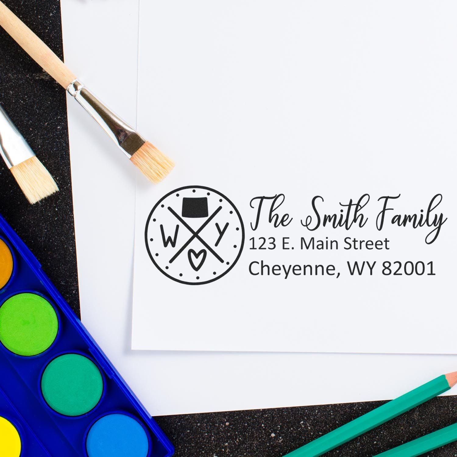 Self-Inking State Love of Wyoming Custom Address Stamp on white paper with The Smith Family address. Surrounded by paintbrushes and watercolor paints, showcasing creative use.