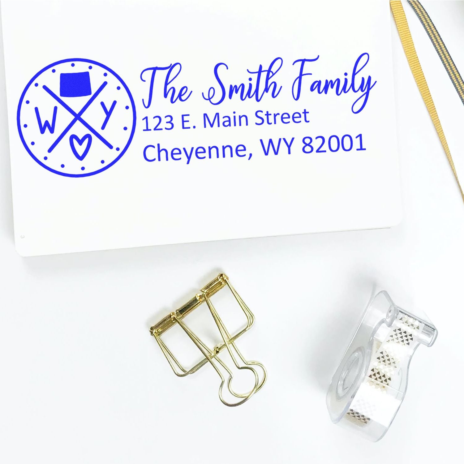 Wyoming State Pride Customized Address Stamp on white paper with The Smith Family and Cheyenne address. Nearby are a gold binder clip and decorative tape.