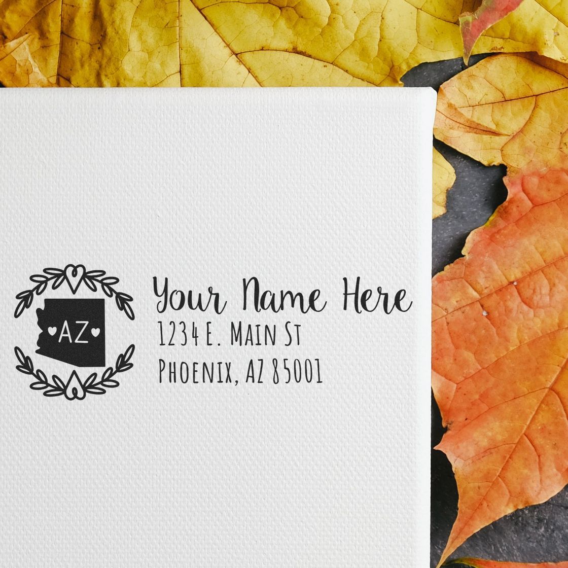 PSI Pre-Inked Arizona State Customized Address Stamp on white paper with autumn leaves. Displays Your Name Here and a sample address in elegant font, featuring an Arizona state outline design.