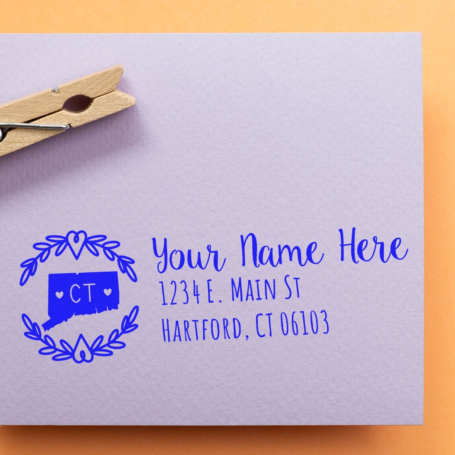 PSI Pre-Inked Connecticut State Customized Address Stamp on a lavender envelope with a blue design, featuring a state outline and address. A wooden clothespin is clipped to the envelope.