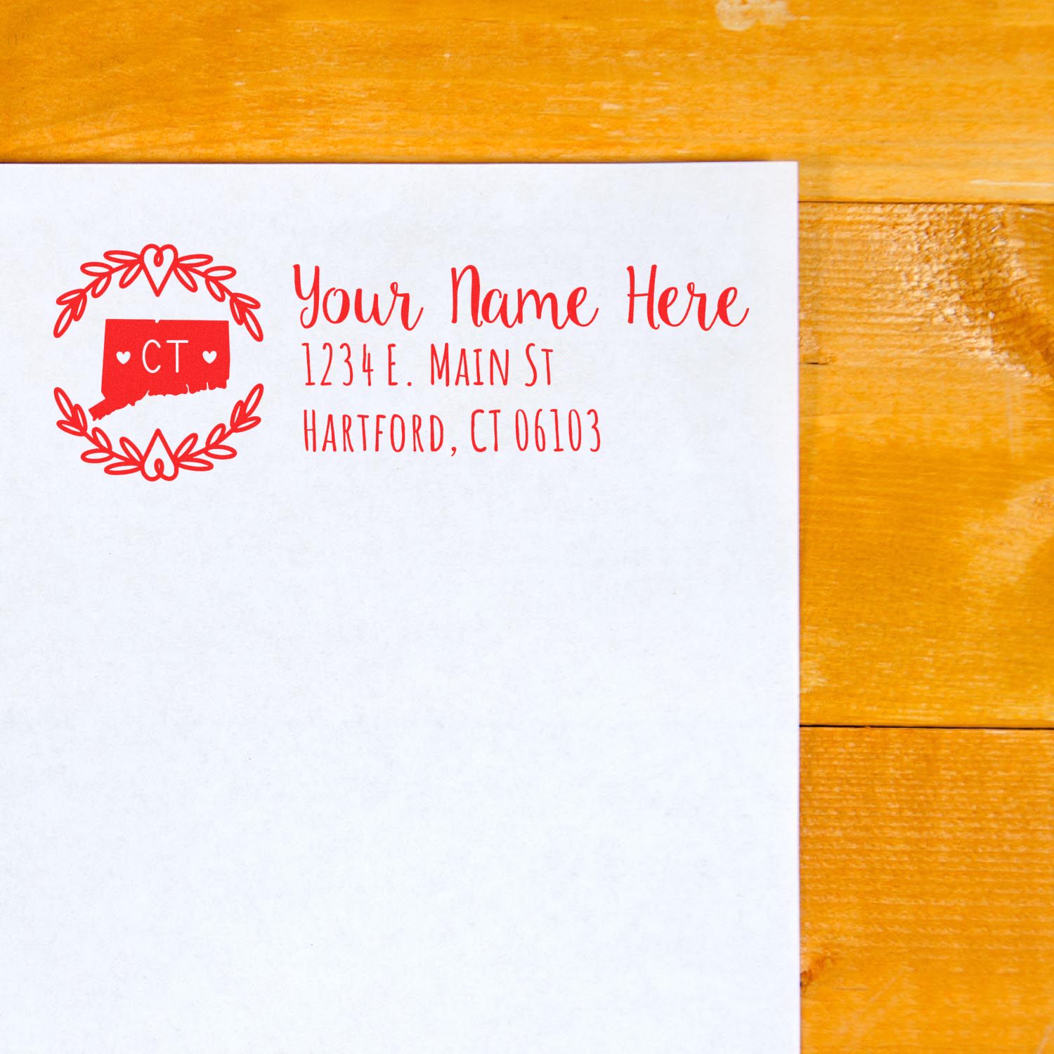 Envelope with a red Connecticut State Custom Return Address Stamp featuring a heart design and placeholder text for name and address, on a wooden surface.