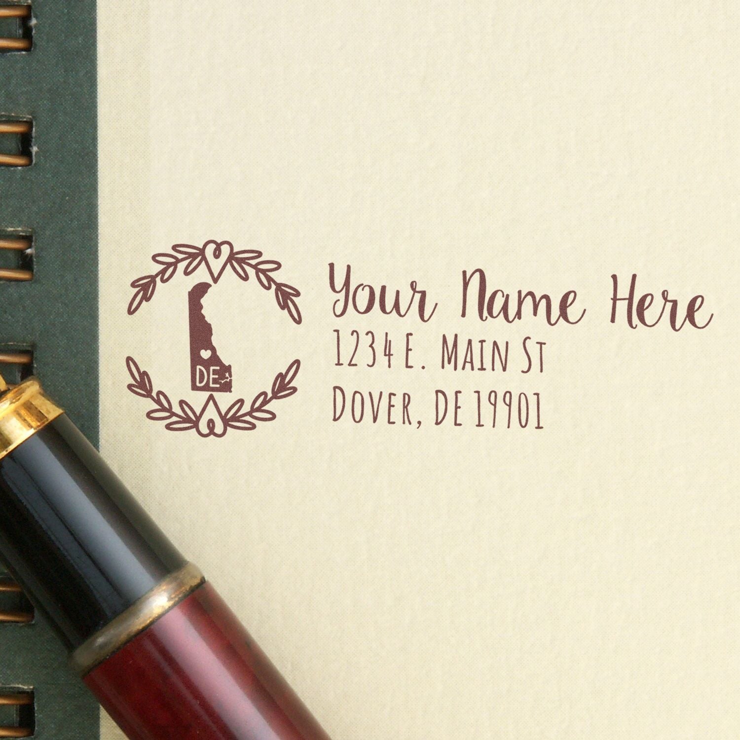 Slim Delaware Personalized Pre-Inked Address Stamp on paper next to a pen, featuring a decorative Delaware state outline and customizable address text. Ideal for personalizing mail with ease.