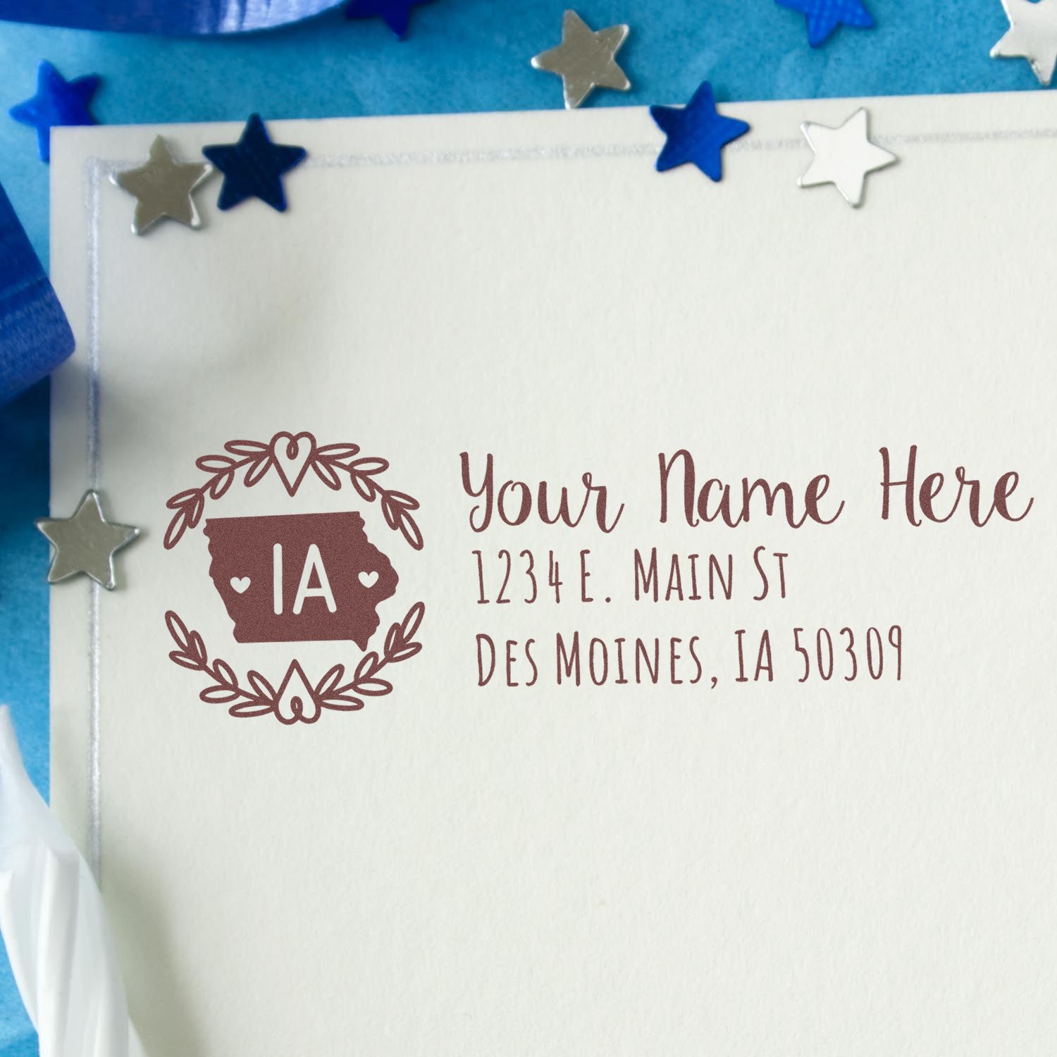 Iowa State Custom Return Address Stamp on an envelope, featuring a decorative Iowa outline with hearts, surrounded by stars and ribbon, displaying a sample address in elegant script.