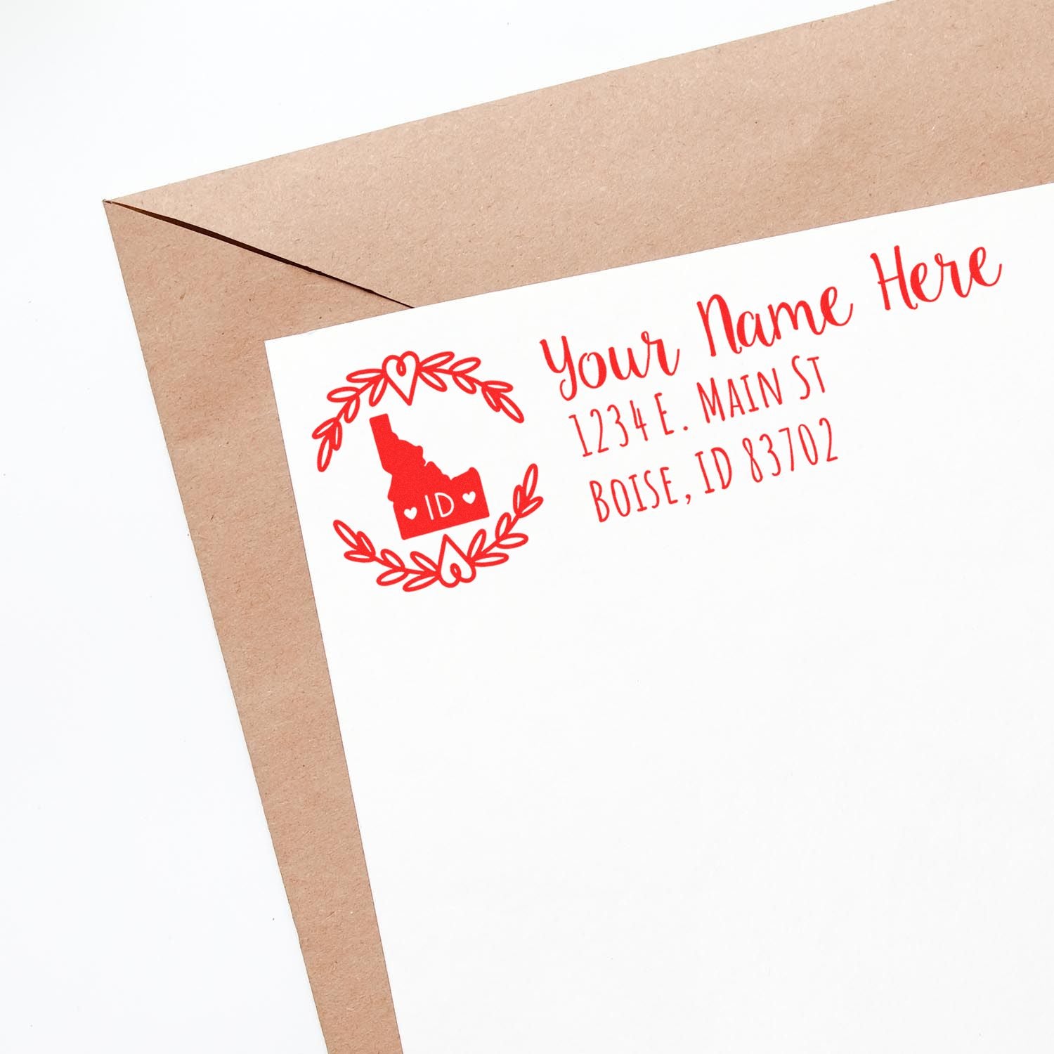 Idaho State Custom Return Address Stamp on a white envelope, featuring a red design with a state outline and laurel wreath, personalized with name and address in red text.