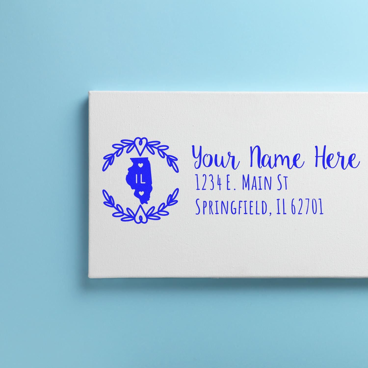 Image of a PSI Pre-Inked Illinois State Customized Address Stamp on a white card with blue text, featuring an outline of Illinois and decorative elements, placed on a light blue background.