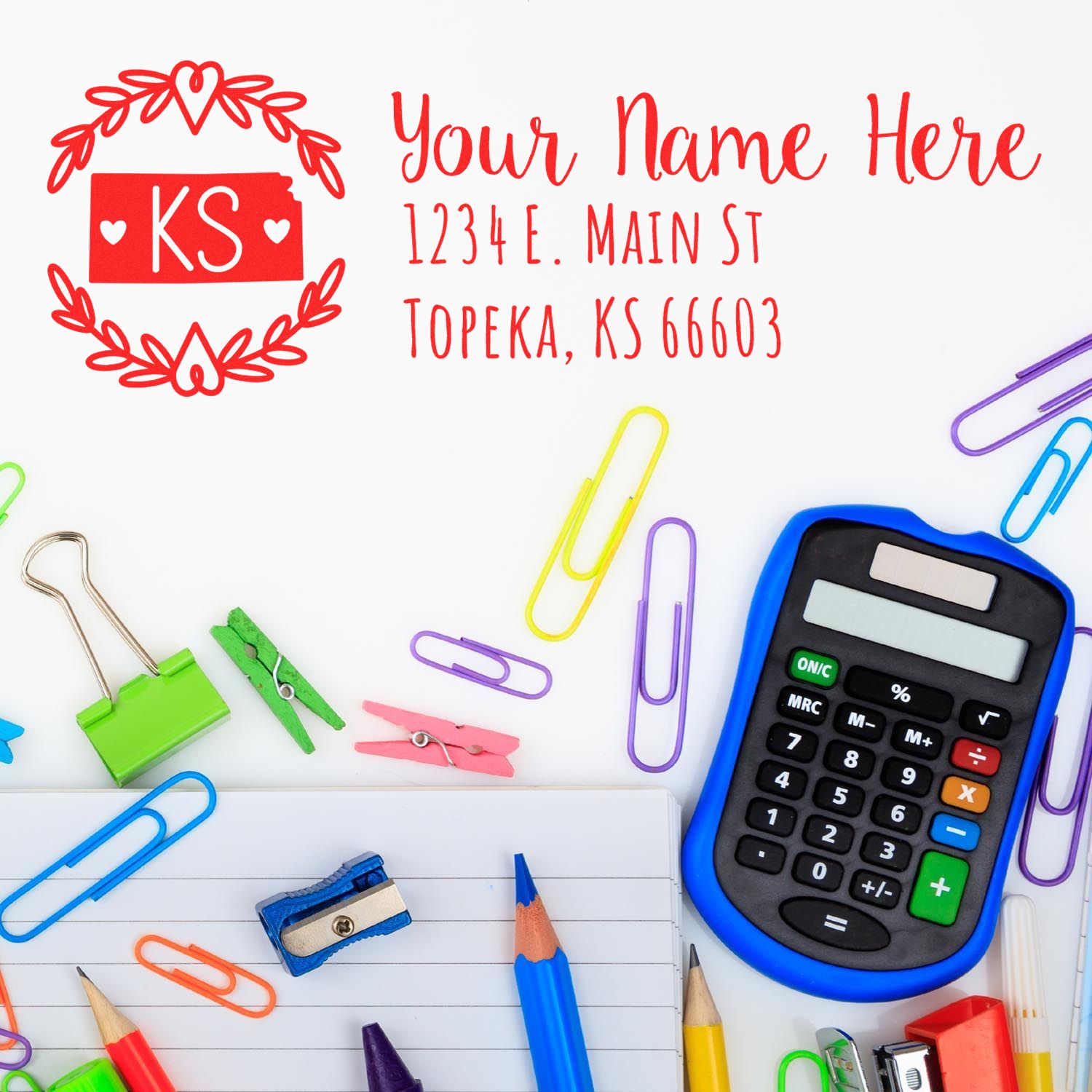 Kansas State Custom Return Address Stamp in red with decorative border, surrounded by colorful office supplies including a calculator, paper clips, and a notepad.