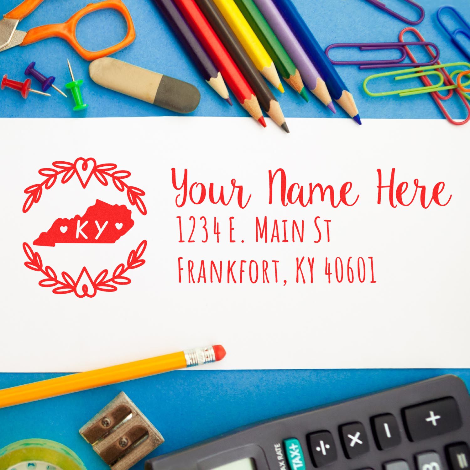 PSI Pre-Inked Kentucky State Customized Address Stamp on white paper, surrounded by colorful office supplies, featuring a red heart design with 'KY' and sample address text.