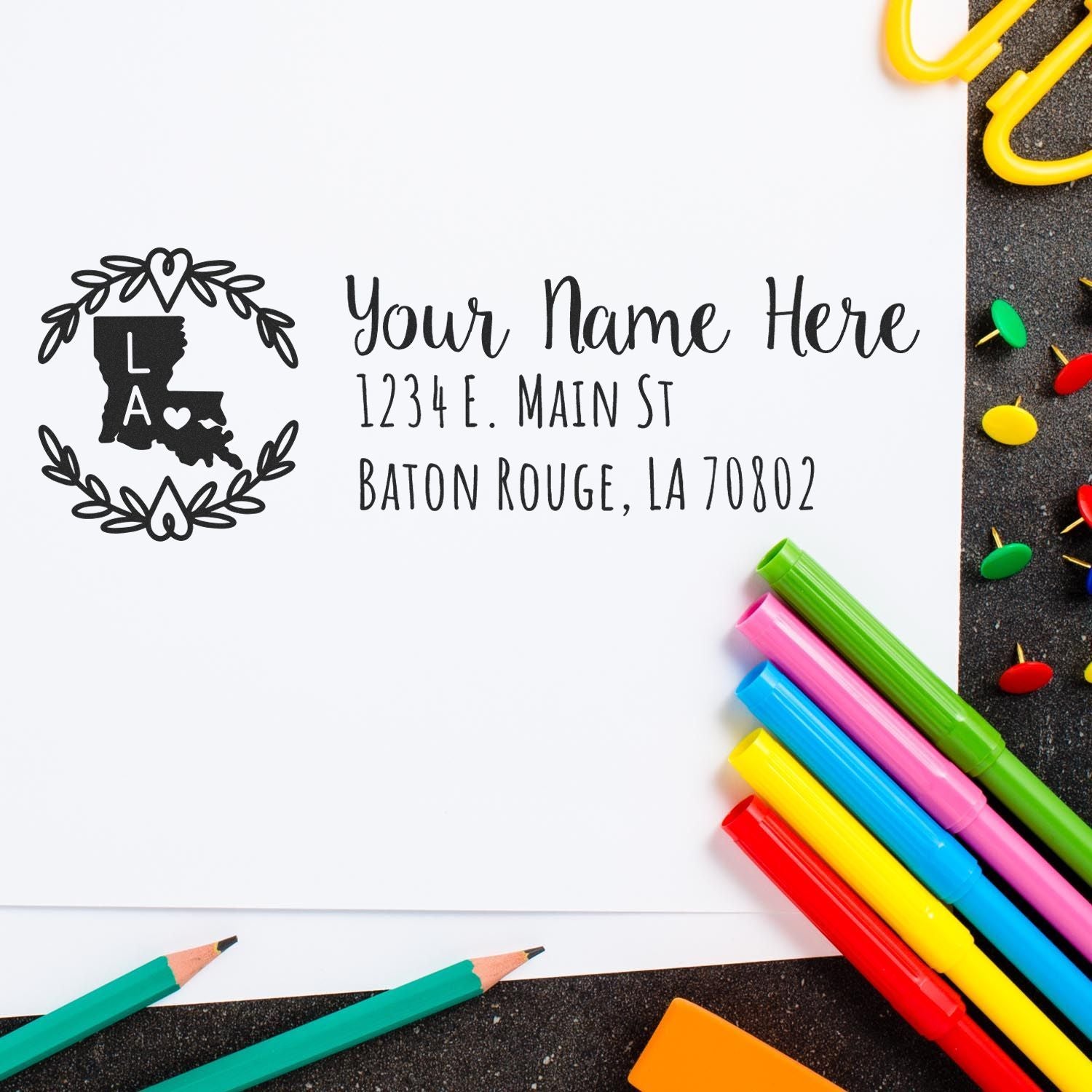 PSI Pre-Inked Louisiana State Customized Address Stamp on white paper, surrounded by colorful pens and paperclips, showcasing a personalized address with a decorative state outline and heart design.