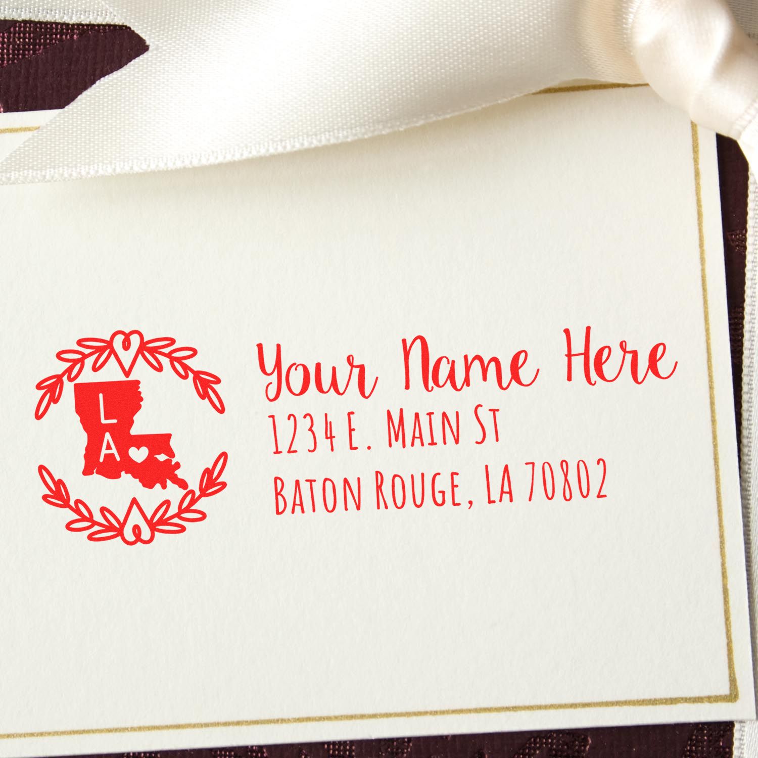 Louisiana State Custom Return Address Stamp on a white card with red text, featuring a state outline and decorative wreath, placed on a textured surface with a white ribbon.