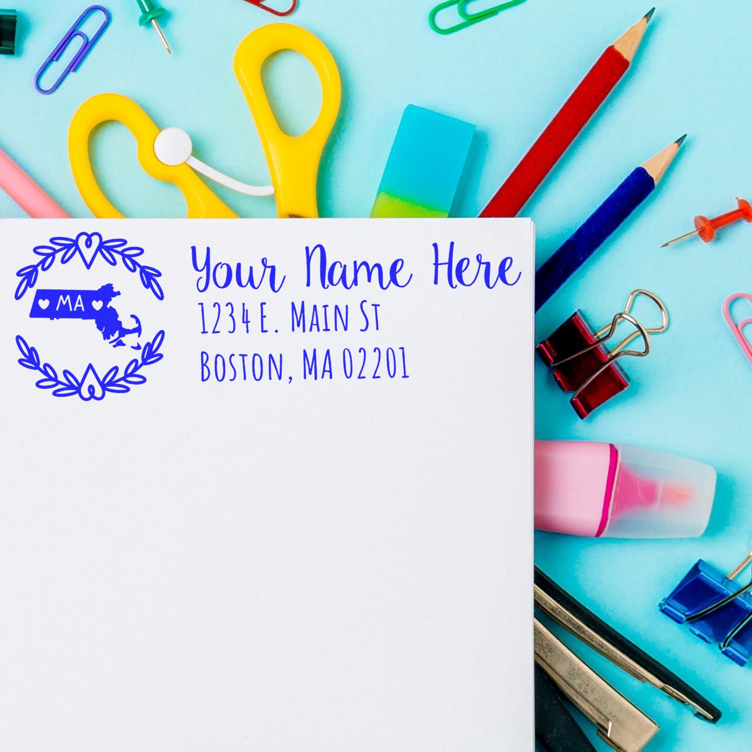 Massachusetts State Custom Return Address Stamp on an envelope surrounded by colorful office supplies, including scissors, pencils, and paper clips, showcasing its elegant design and functionality.