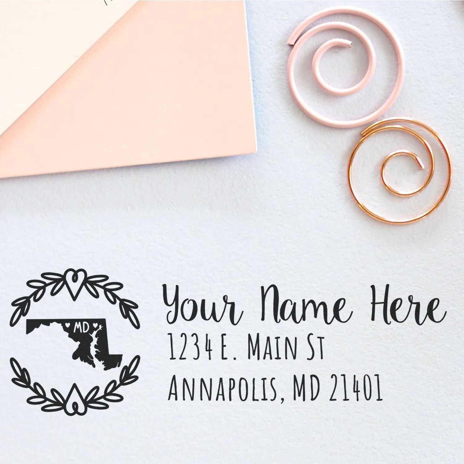 Maryland State Custom Return Address Stamp on a light surface with envelopes and decorative spirals, featuring a Maryland map design and personalized address text.