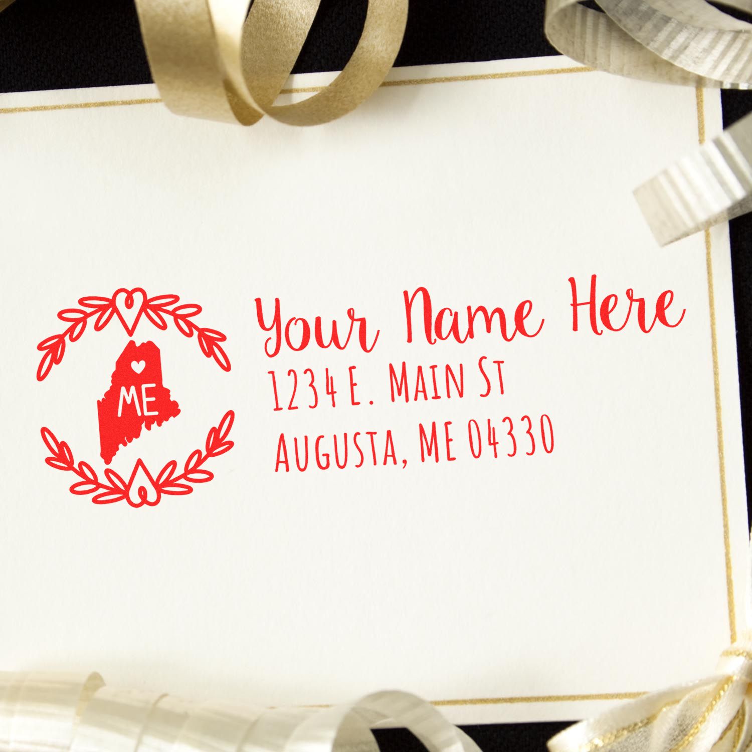 Self-Inking State Wreath of Maine Address Stamp on a white card with red text, featuring a Maine state outline and decorative wreath. Surrounded by gold and silver ribbons.