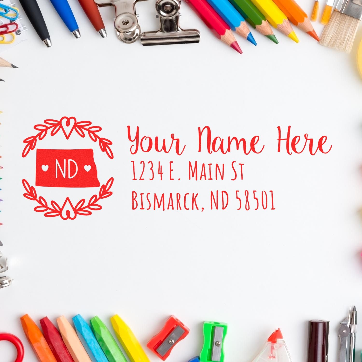 A red Self-Inking State Wreath of North Dakota Address Stamp imprint on white paper, surrounded by colorful stationery items like pencils, markers, and clips.