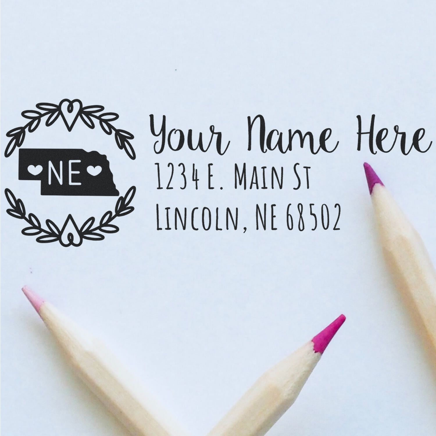 Slim Nebraska Personalized Pre-Inked Address Stamp on white paper with a decorative Nebraska state outline, customizable text, and two pencils with pink tips nearby.