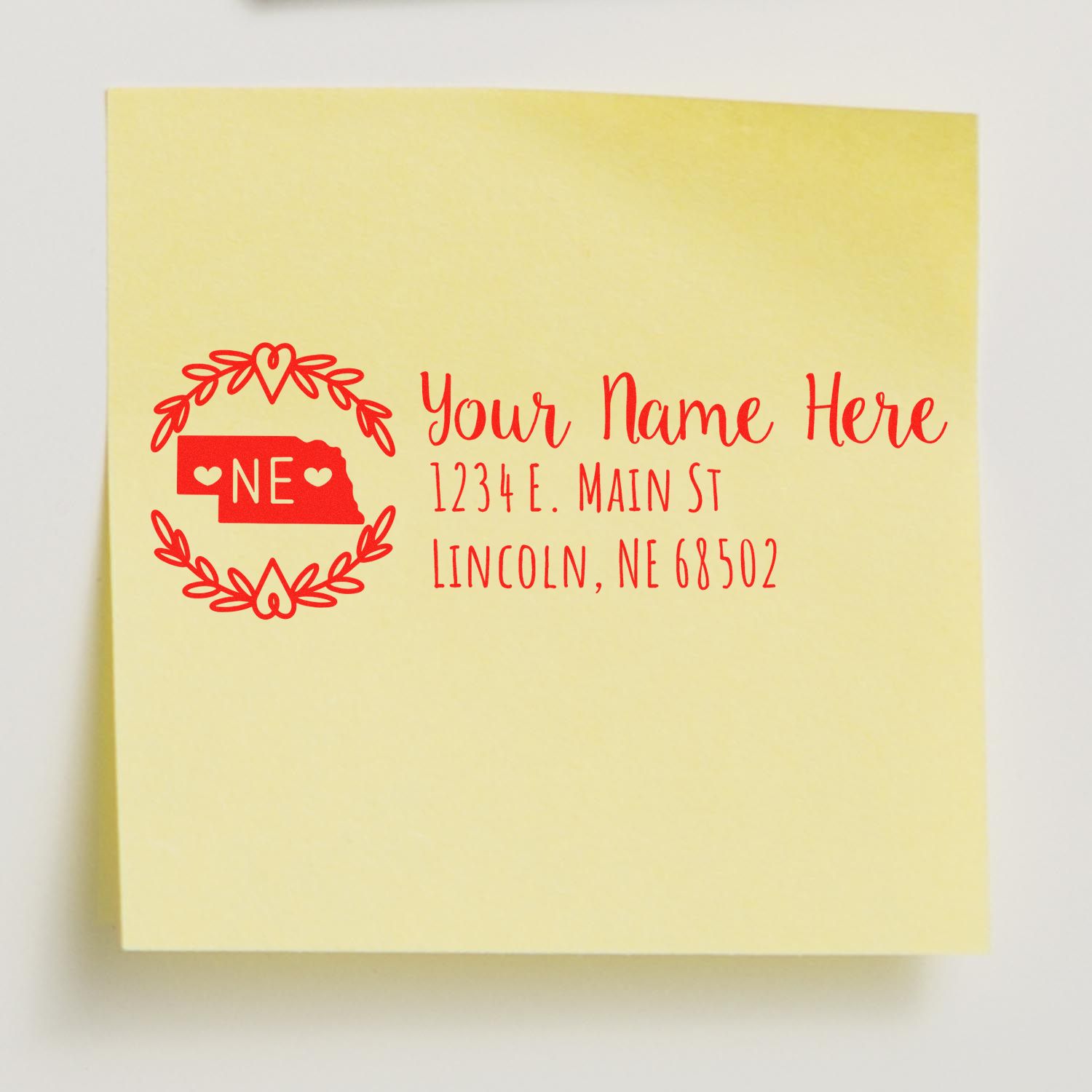 Yellow sticky note with red ink from the Slim Nebraska Personalized Pre-Inked Address Stamp, featuring a decorative border, placeholder text for name, street, and Lincoln, NE address.