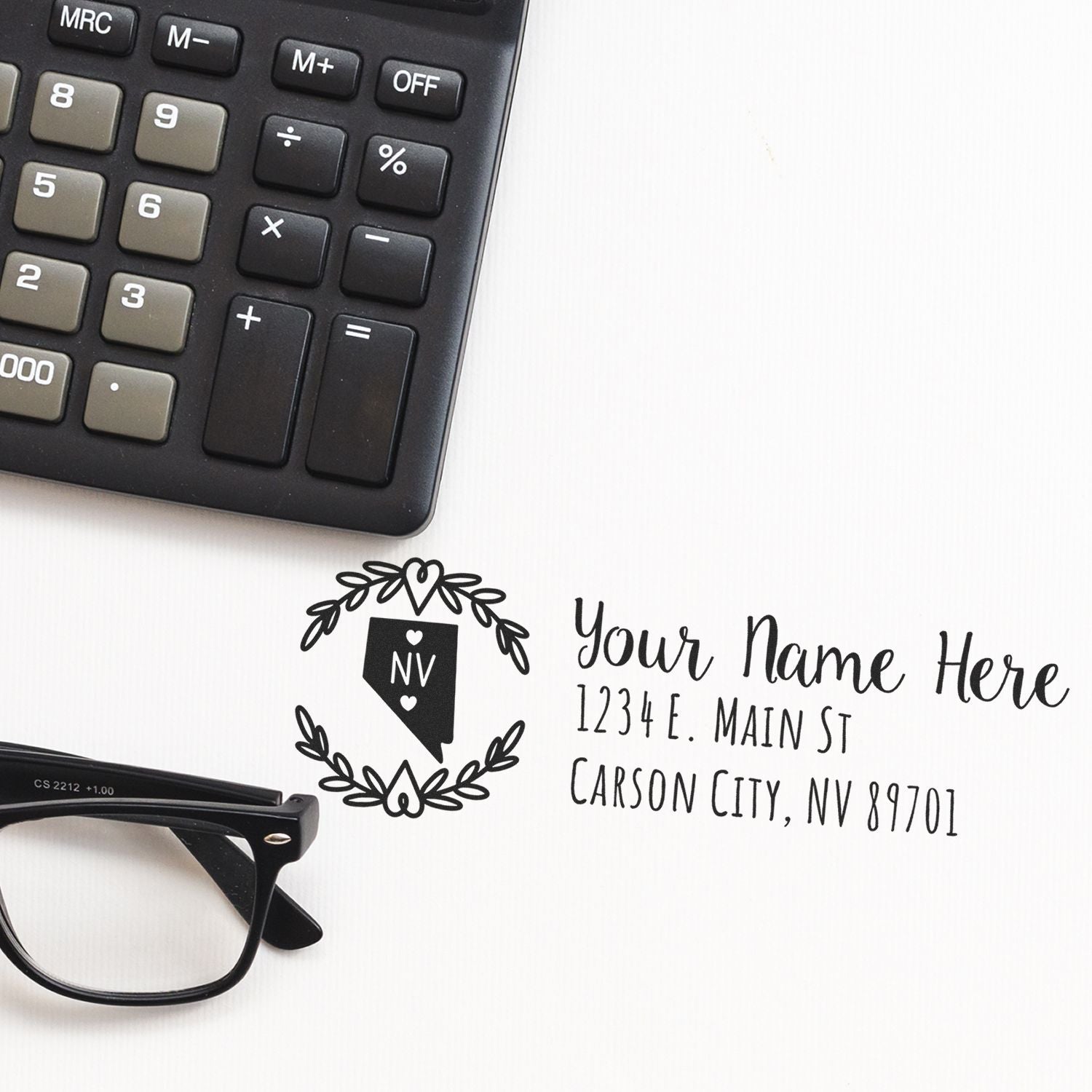 A Self-Inking State Wreath of Nevada Address Stamp on paper next to a calculator and glasses, displaying a sample address with a decorative Nevada state emblem.