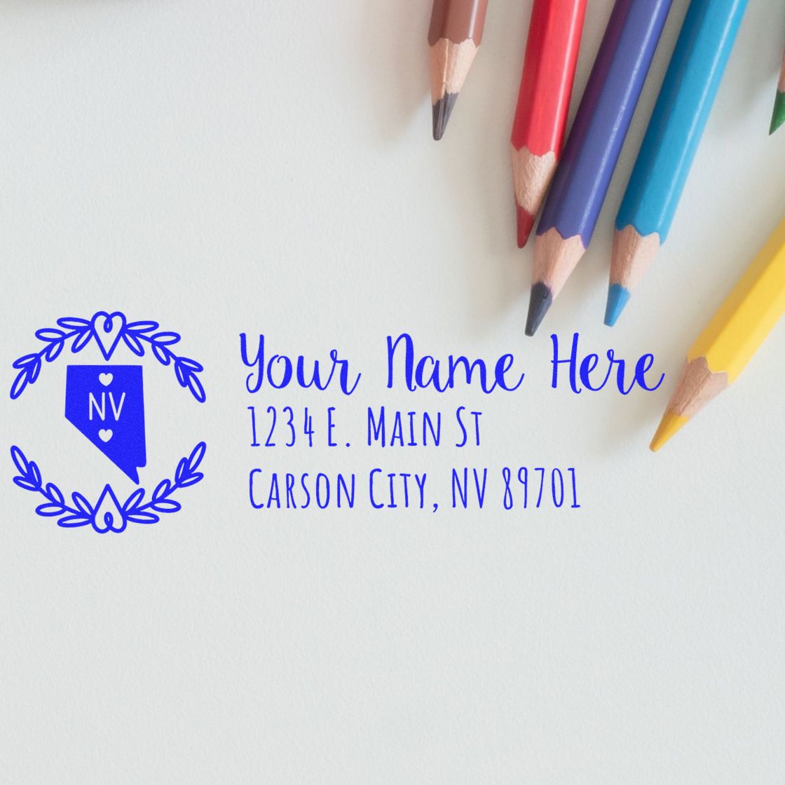 Self-Inking State Wreath of Nevada Address Stamp on paper with colorful pencils. Displays Your Name Here and a sample address in blue ink, featuring a Nevada state outline with a wreath design.