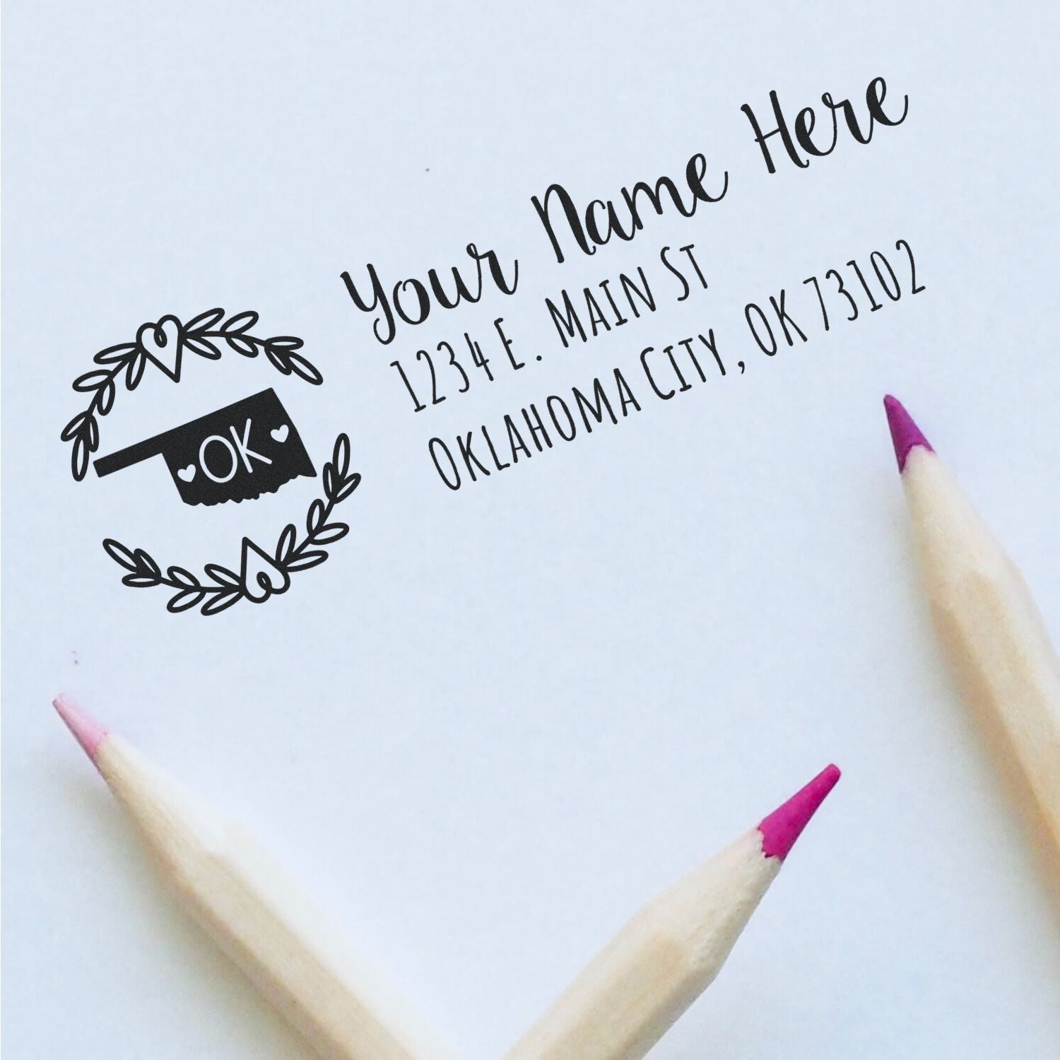 Oklahoma State Custom Return Address Stamp on white paper with decorative heart border, featuring placeholder text for name and address. Two pencils with pink tips are nearby.