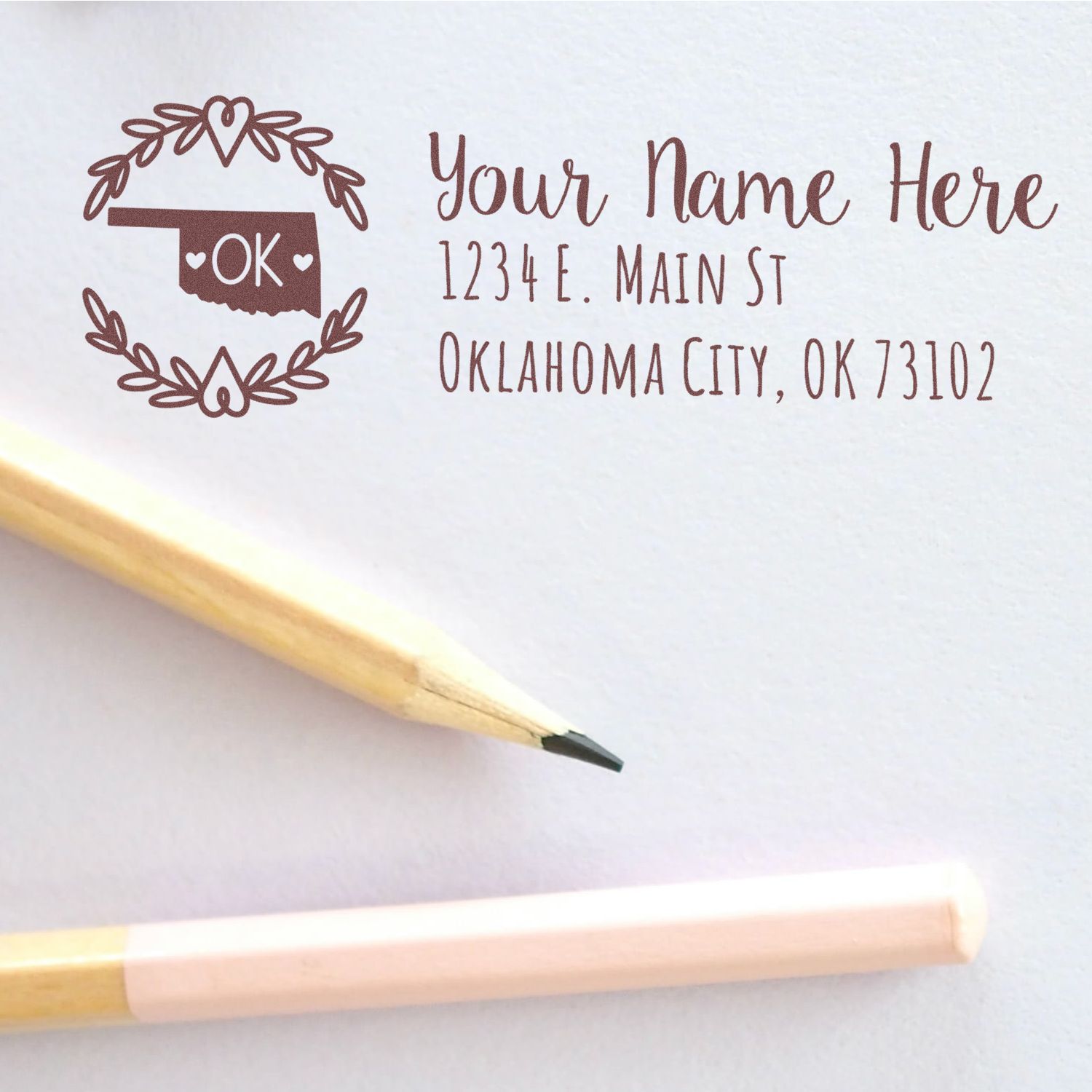 Oklahoma State Custom Return Address Stamp on white paper, featuring a decorative state outline with OK and floral accents, next to two pencils.